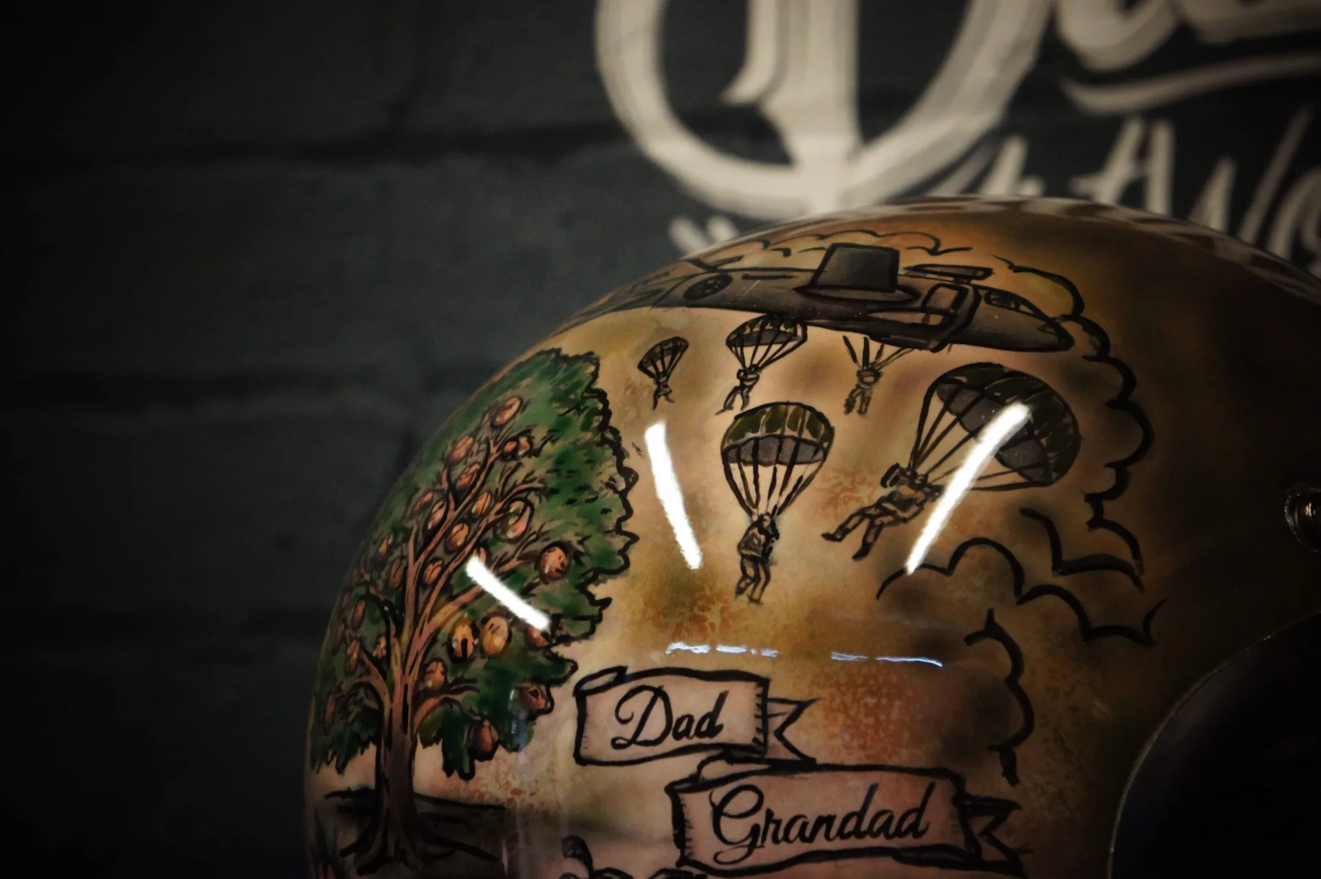 Rear of the finished helmet showing the Malaysia banner, a hand-painted Land Rover and vintage motorcycle among clouds and flowers on an aged-gold base.