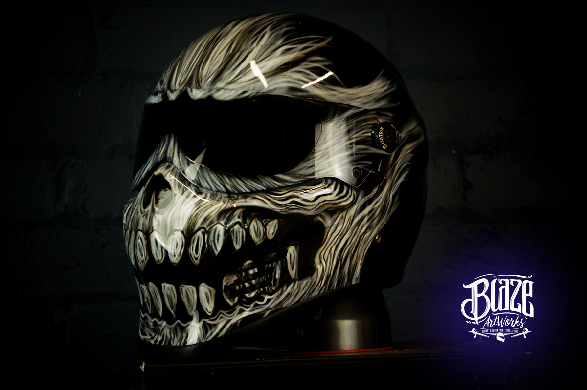 Motorcycle helmet with intricate carved bone skull design featuring flowing cream and brown carved patterns with menacing teeth