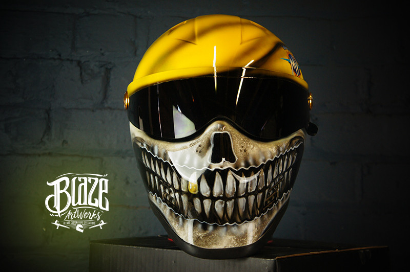 Yellow motorcycle helmet with detailed black and white skull jaw design painted across the face shield area