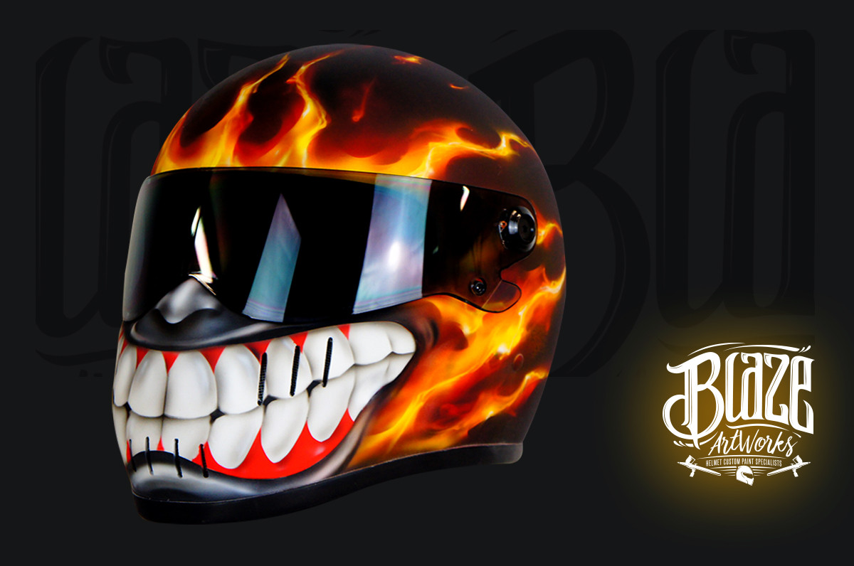 Motorcycle helmet with fiery orange flame paint and menacing white fanged teeth design on black background with mirrored visor