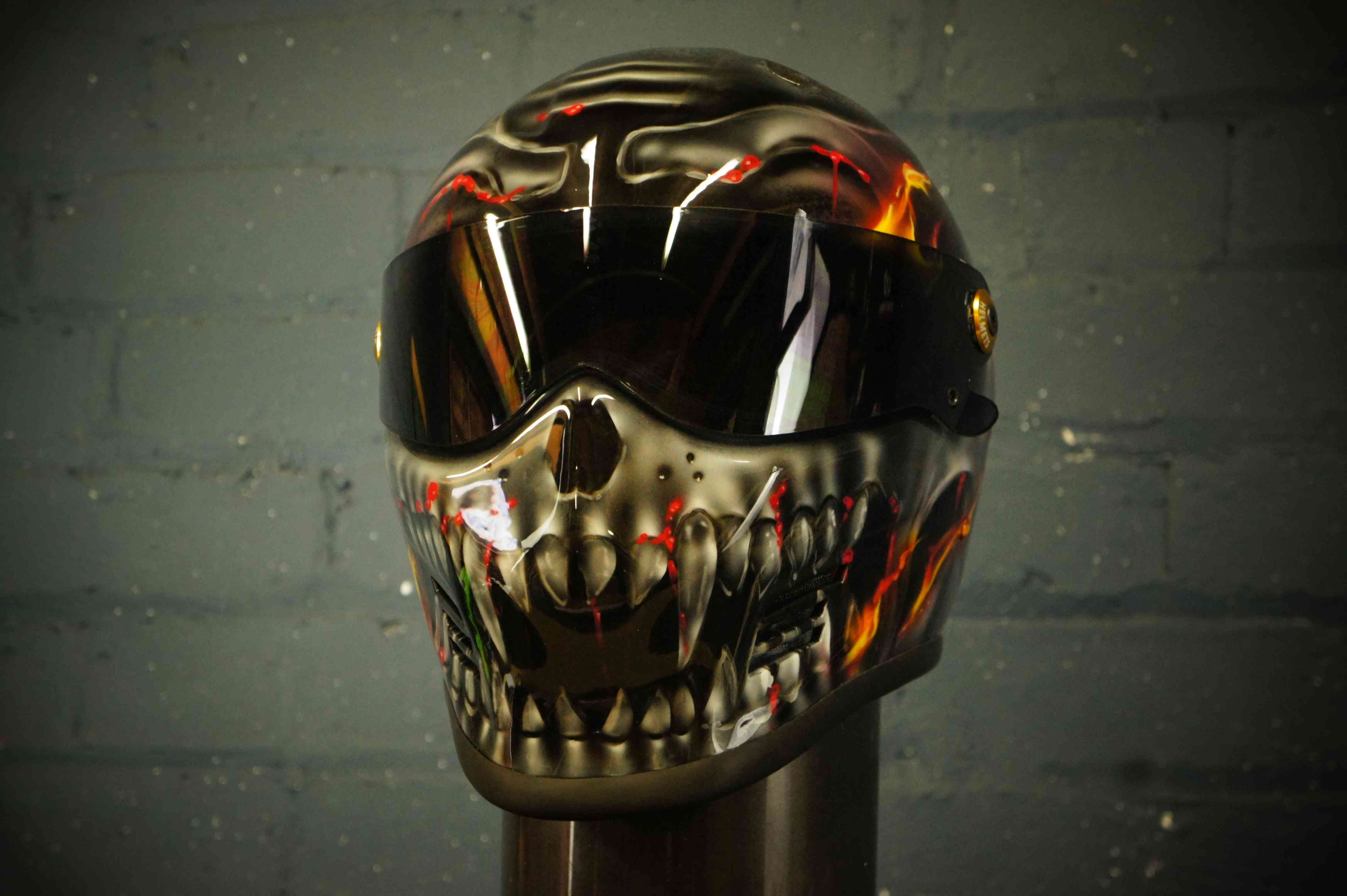 Black motorcycle helmet with realistic flaming skull design featuring orange red flames yellow accents and detailed skeleton jaw artwork