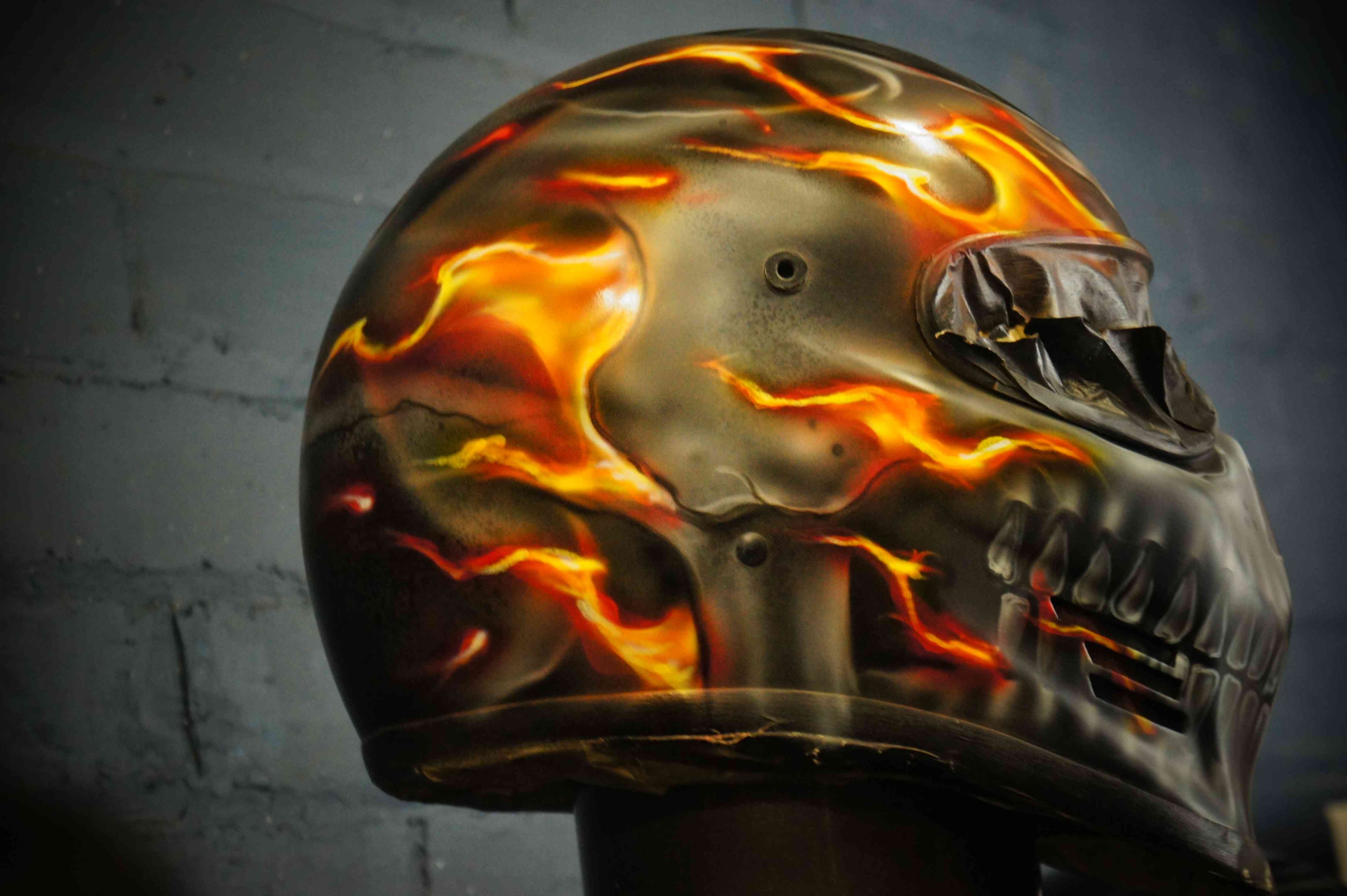 Custom painted motorcycle helmet featuring photorealistic skull design with orange and yellow ghost flames flowing across black surface