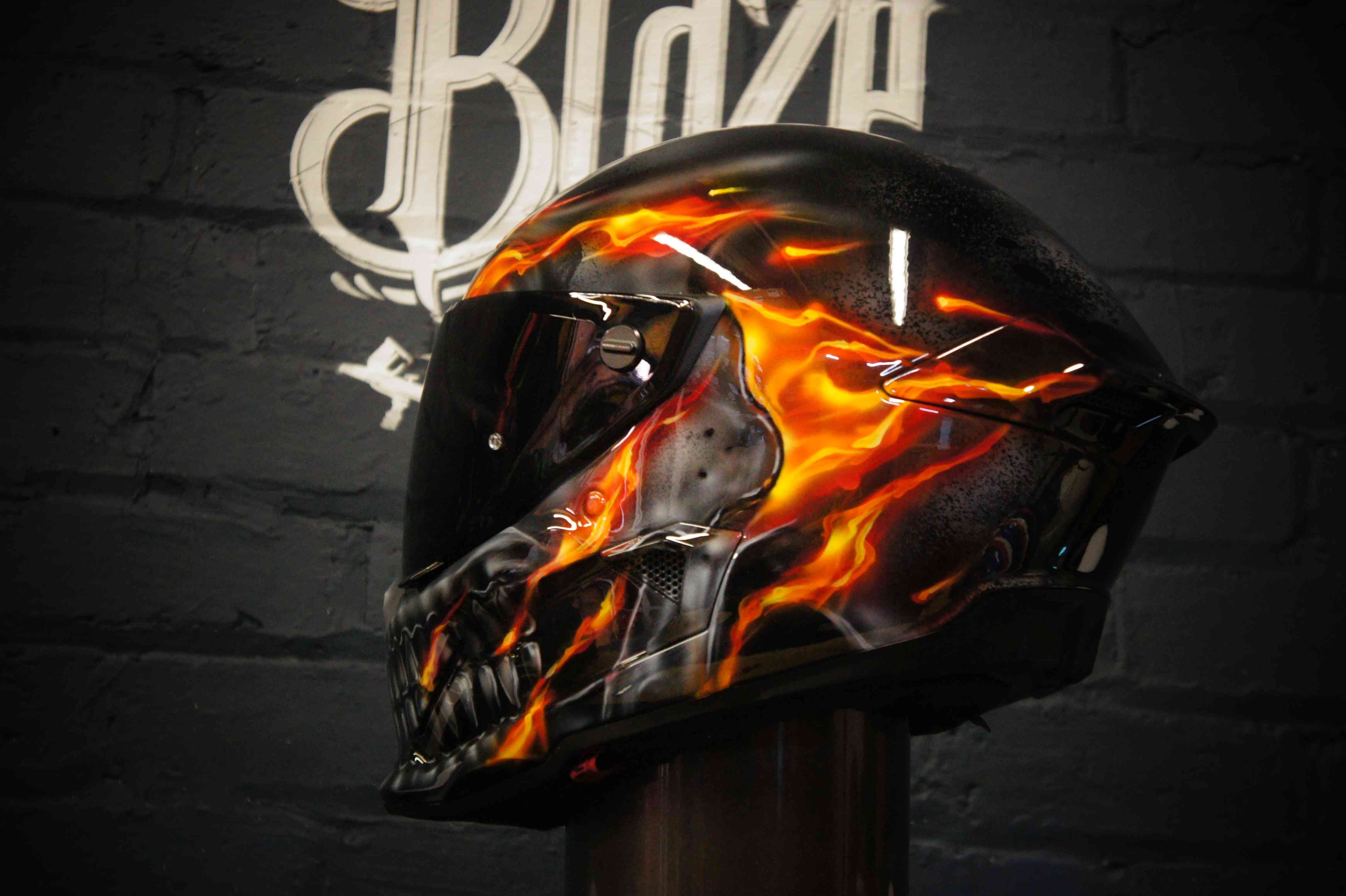 Black motorcycle helmet with realistic orange and yellow flame airbrush design engulfing grey skull artwork on side panel