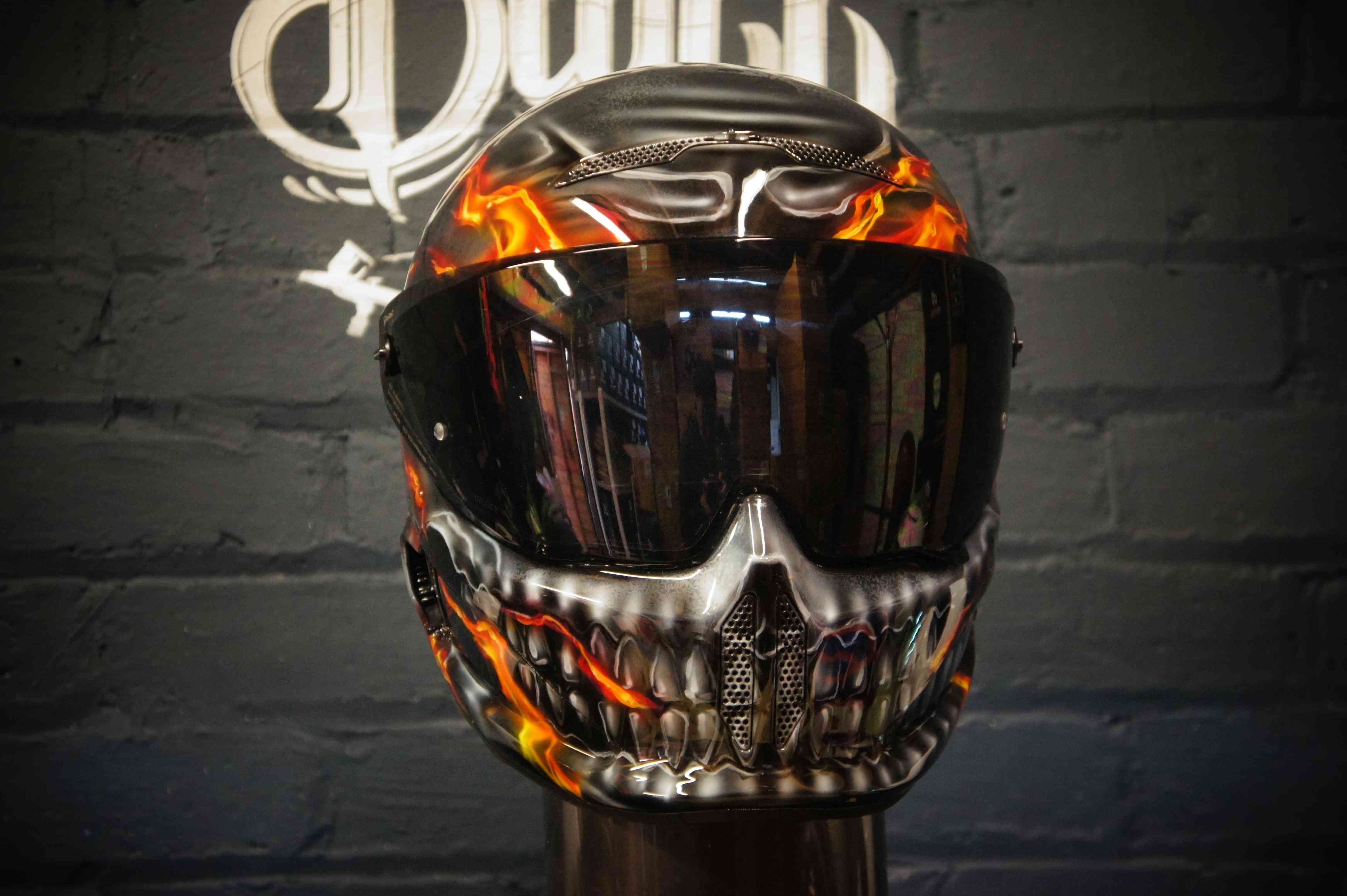 Black motorcycle helmet with orange flame skull design, metallic silver jaw detail, dark tinted visor, professional airbrush work