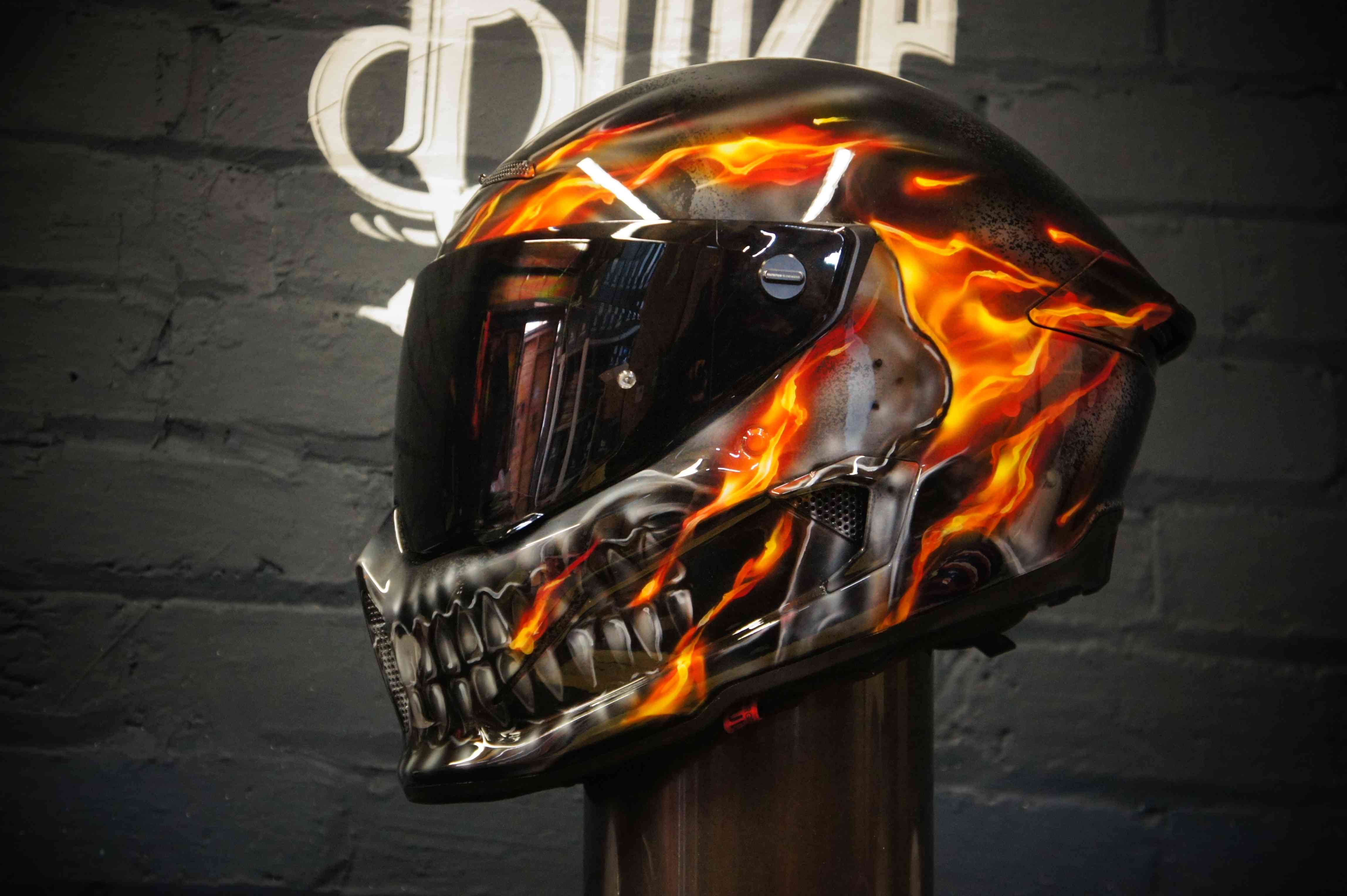 Black motorcycle helmet with realistic orange flame design and metallic skull graphic, featuring detailed airbrush work