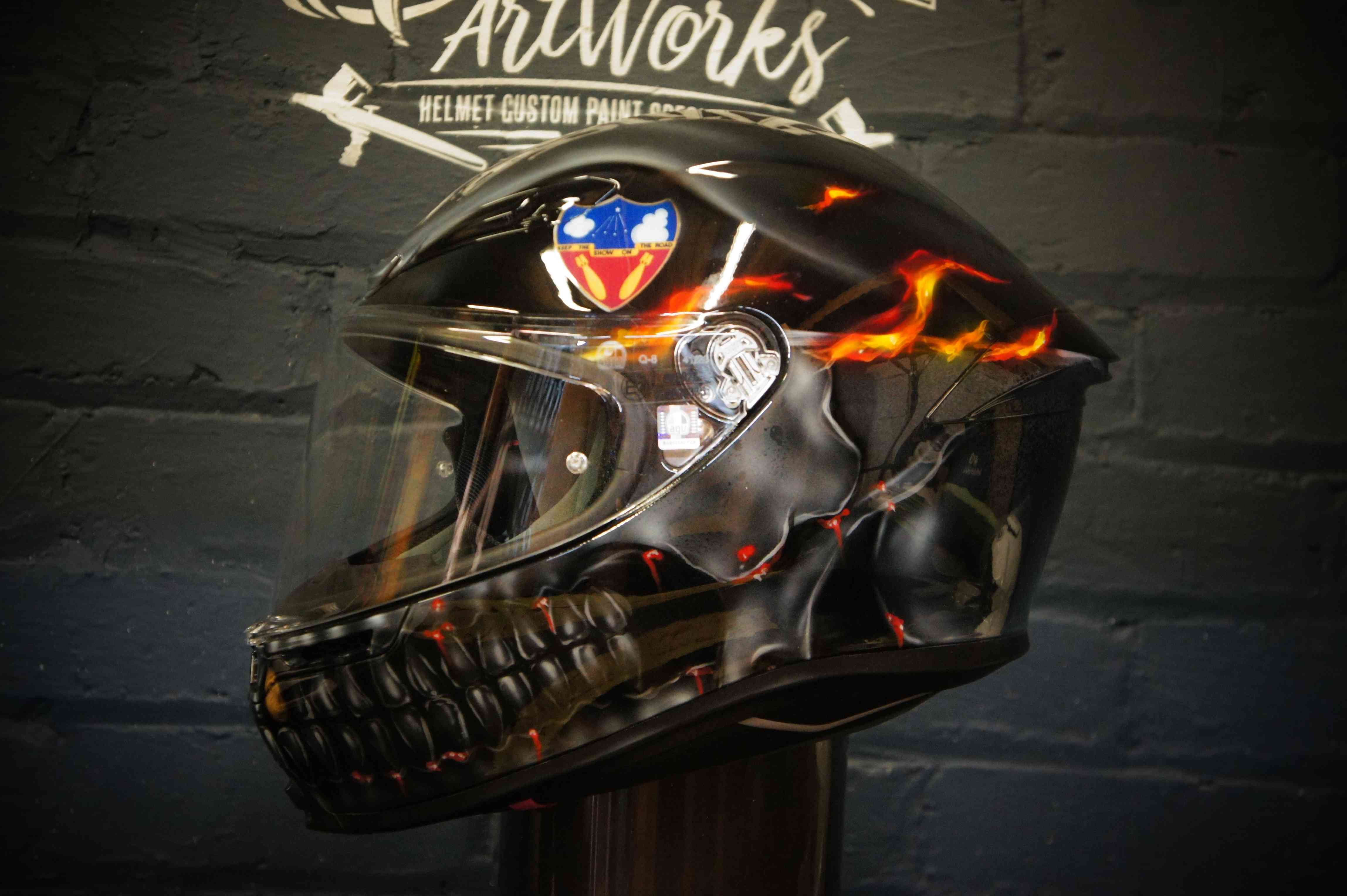 Black motorcycle helmet with airbrushed flaming skull jaw design and glowing orange fire effects on glossy finish