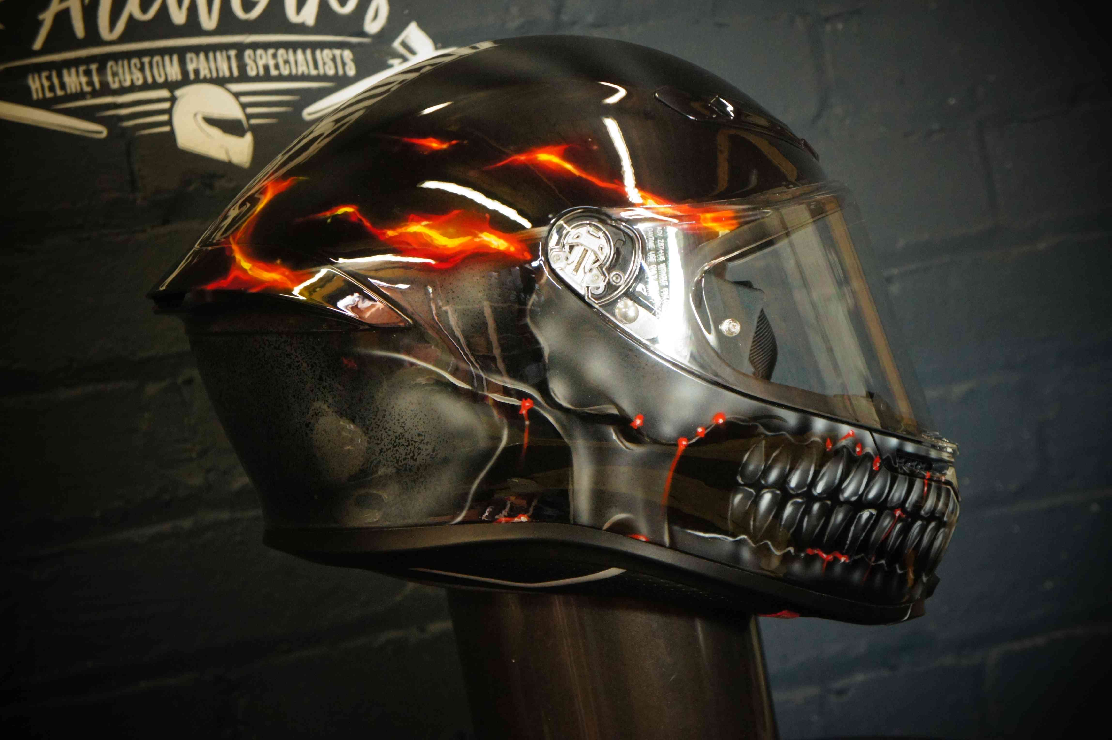 Black motorcycle helmet with realistic orange and red flames flowing over detailed skull design, featuring skeletal jaw