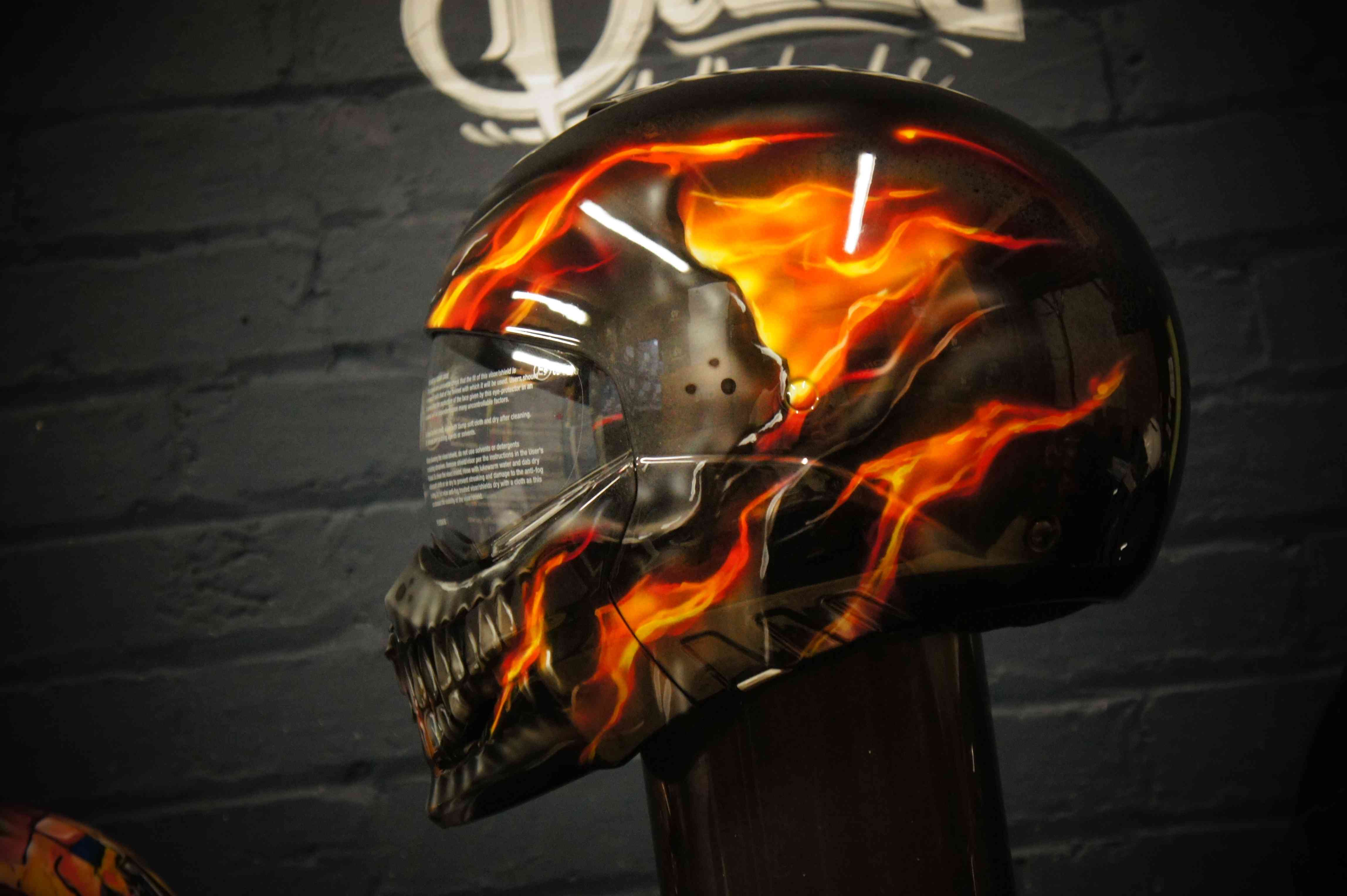 Black motorcycle helmet with realistic orange and red flames surrounding detailed chrome skull artwork in photorealistic style