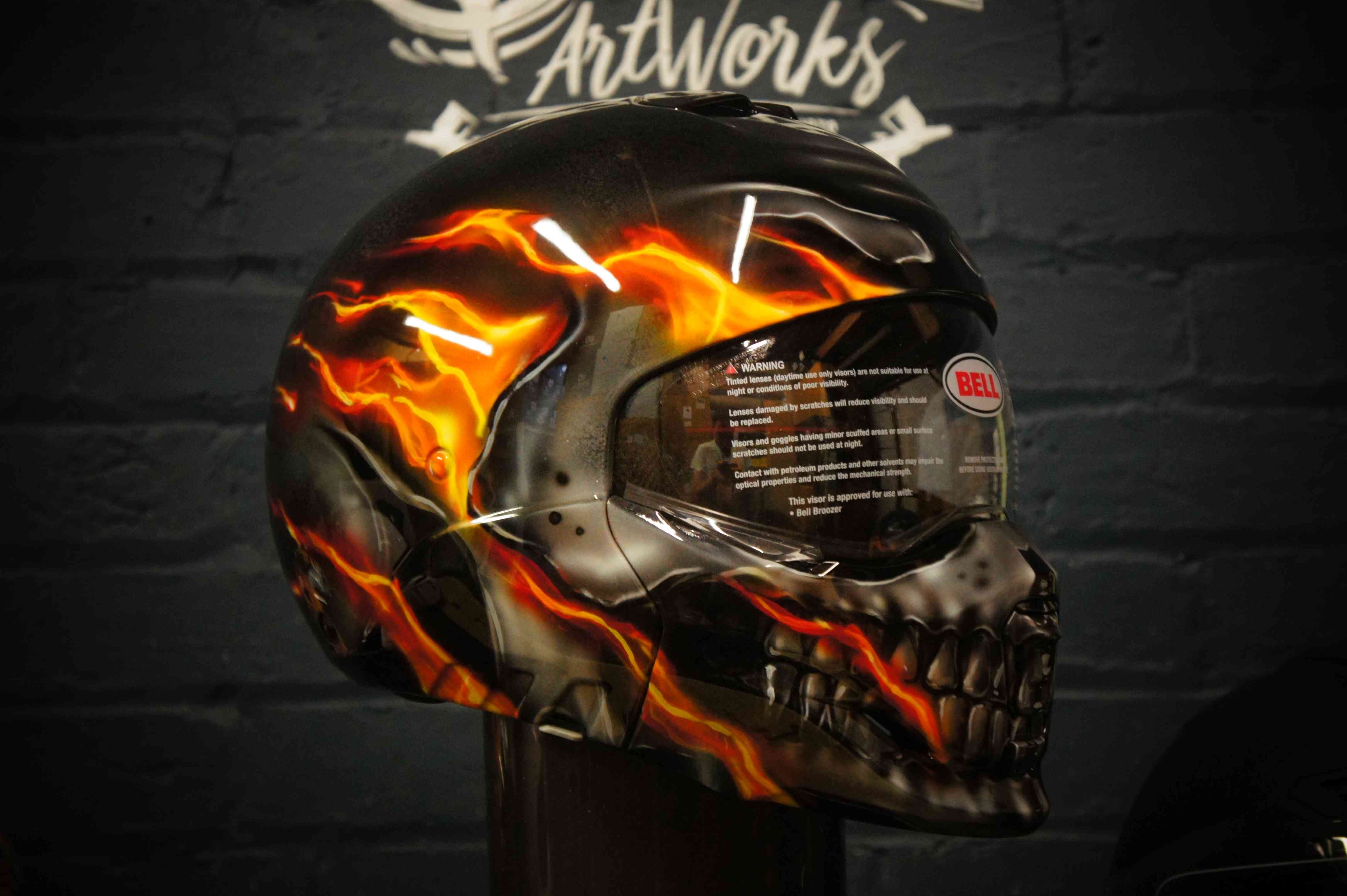 Black motorcycle helmet with realistic flaming skull design in orange and yellow flames, detailed teeth and eye sockets