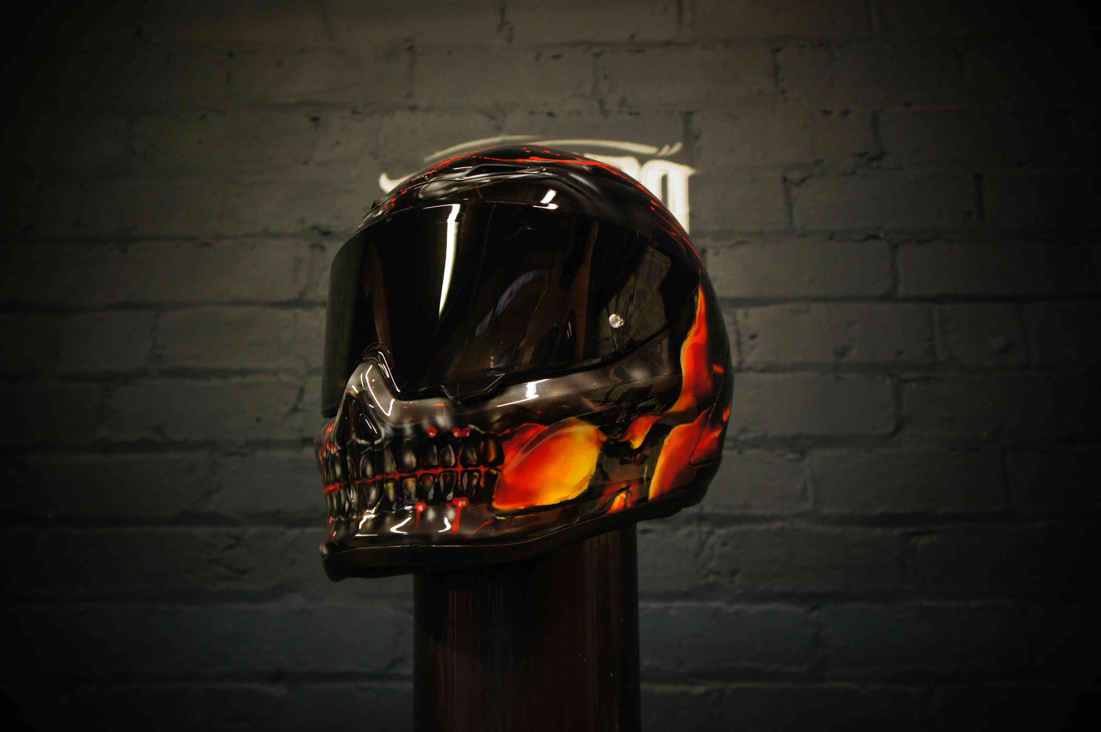 Black motorcycle helmet with photorealistic airbrushed skull design featuring orange and red flame effects around eye sockets