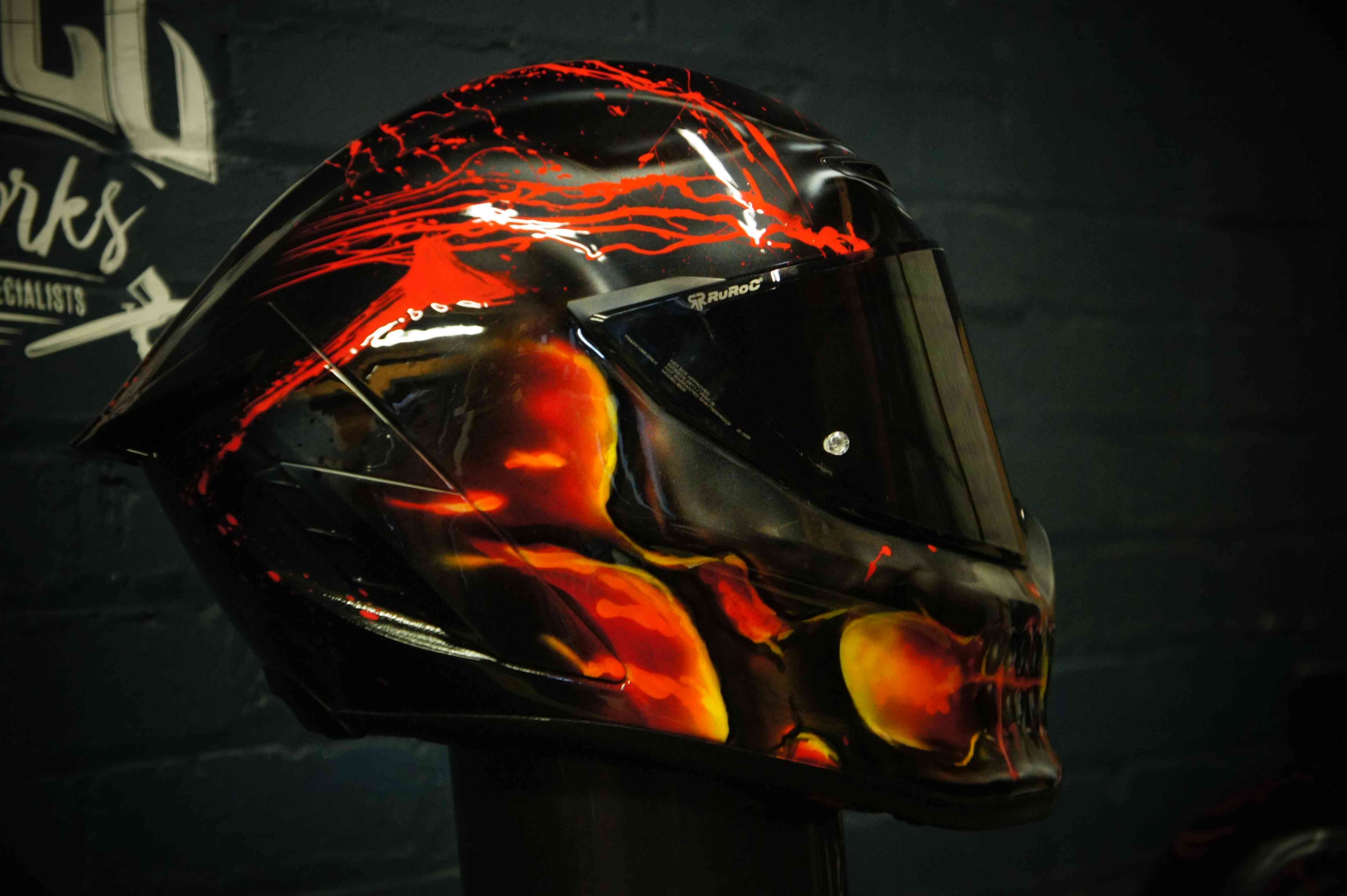 Black motorcycle helmet featuring dramatic red and orange flames with menacing skull face design, glossy professional finish