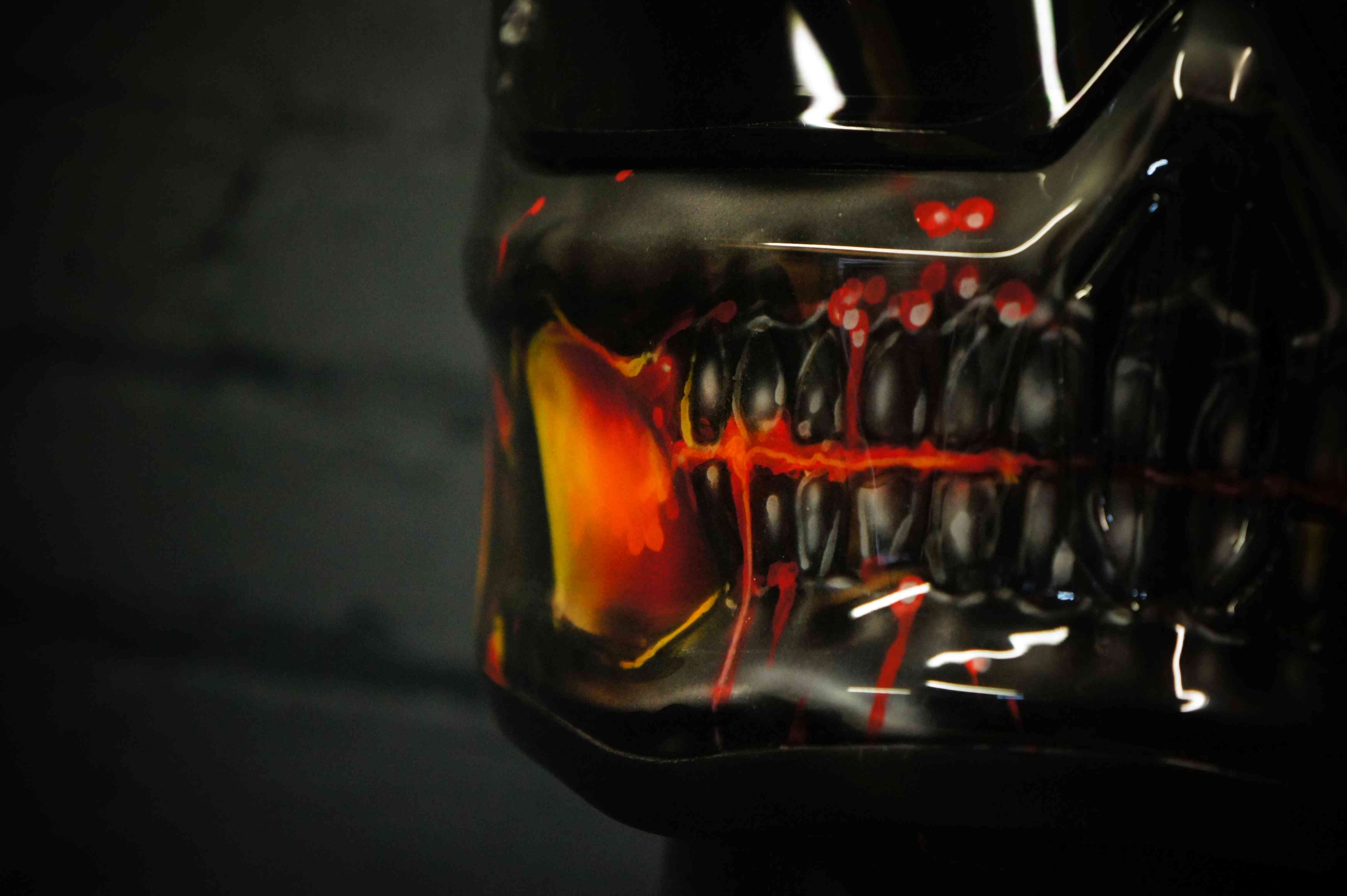 Black motorcycle helmet with menacing skull design featuring fiery orange interior mouth, sharp teeth, and glowing red accents