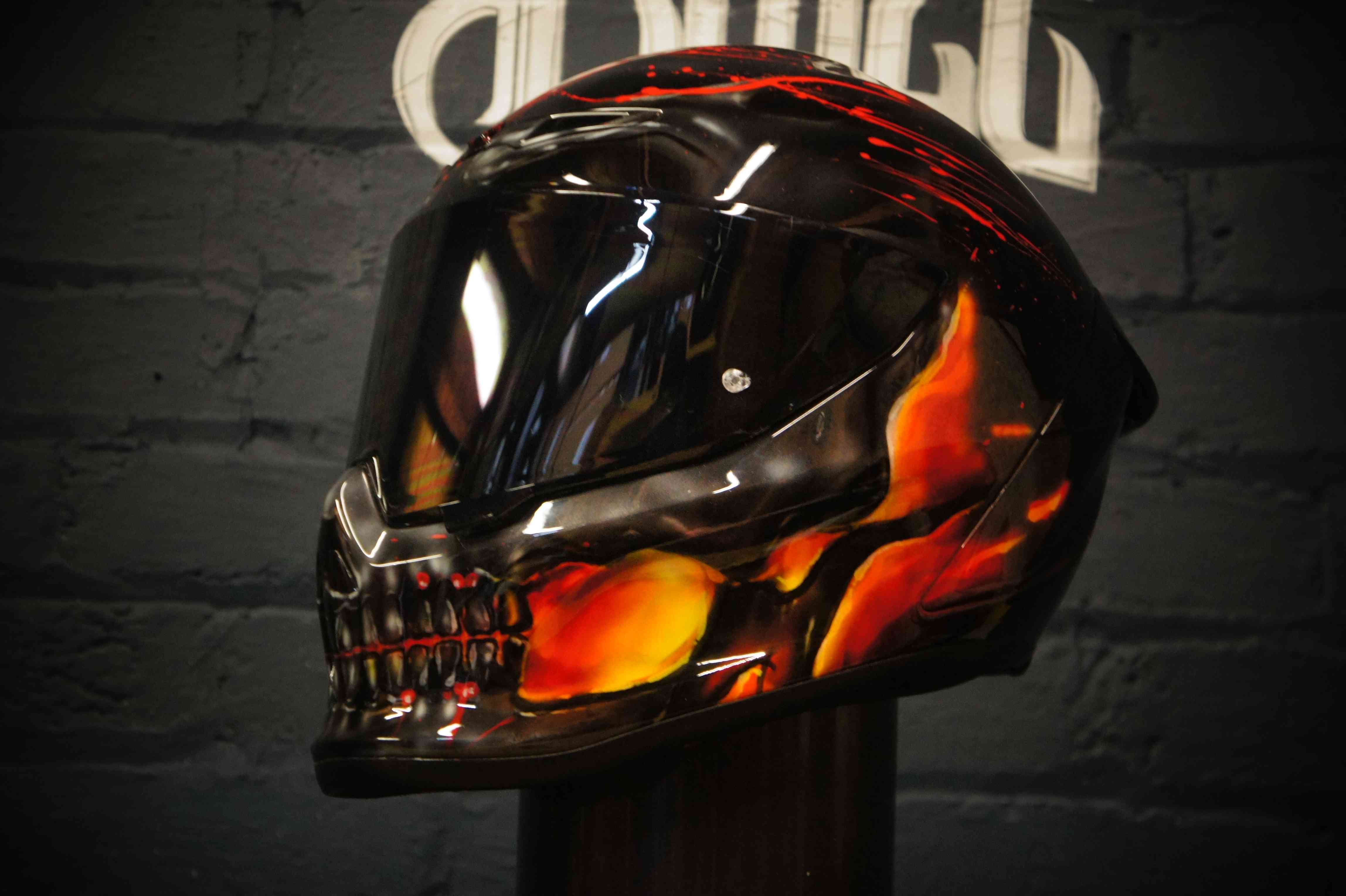 Black motorcycle helmet with realistic orange and red flames surrounding a detailed skull design with glowing eye sockets