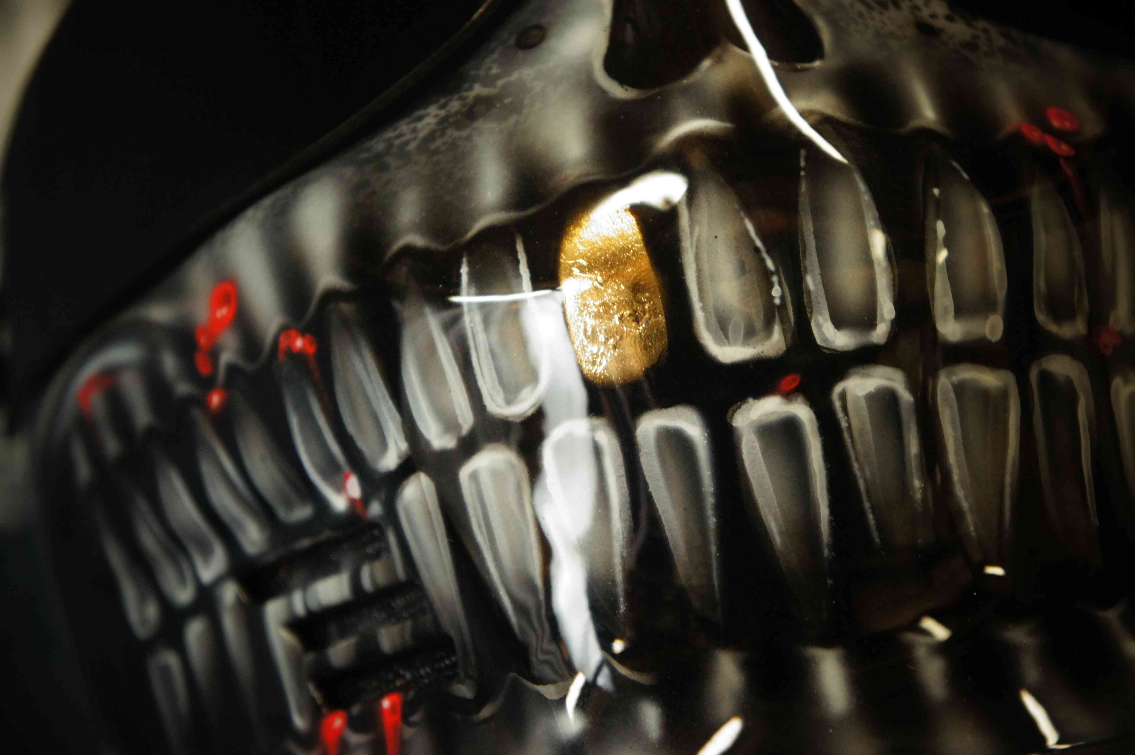 Close-up of motorcycle helmet with realistic 3D skull jaw design in black and gold, showing detailed teeth and bone structure