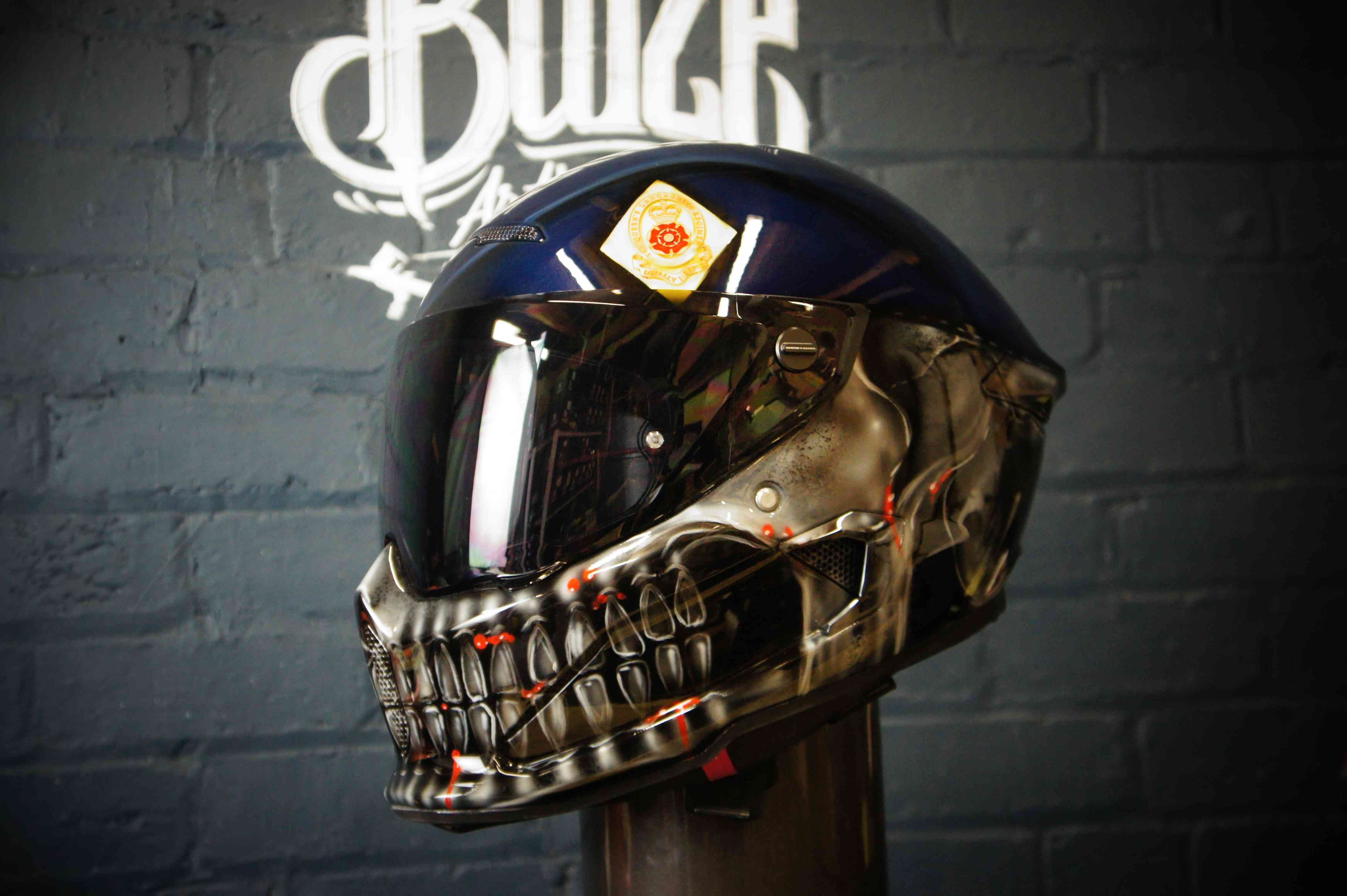 Black motorcycle helmet with photorealistic metallic skull design featuring glowing red accents and anatomical detail work