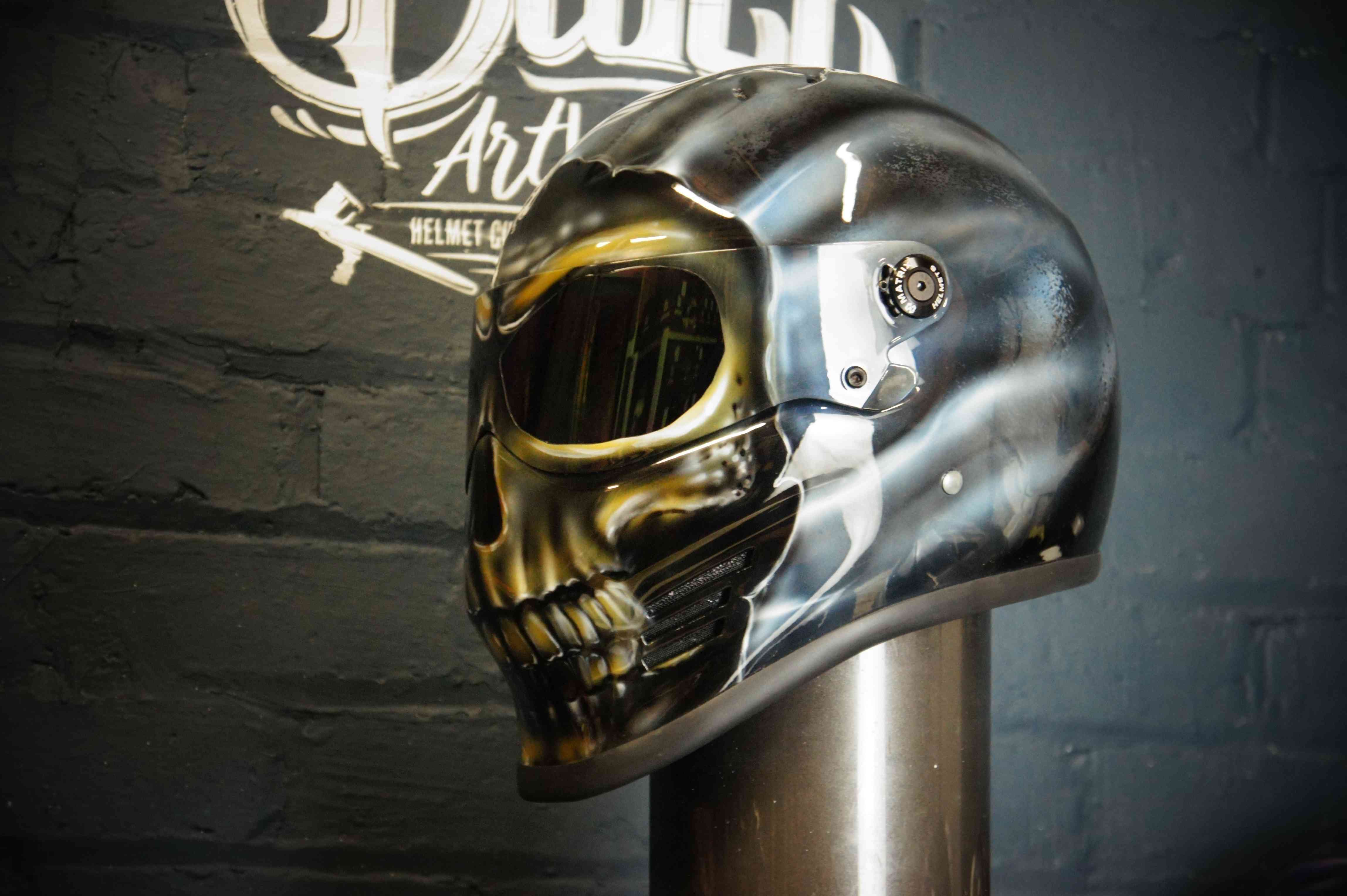 Chrome silver motorcycle helmet with airbrushed skull jaw design featuring golden eye sockets and realistic bone detail