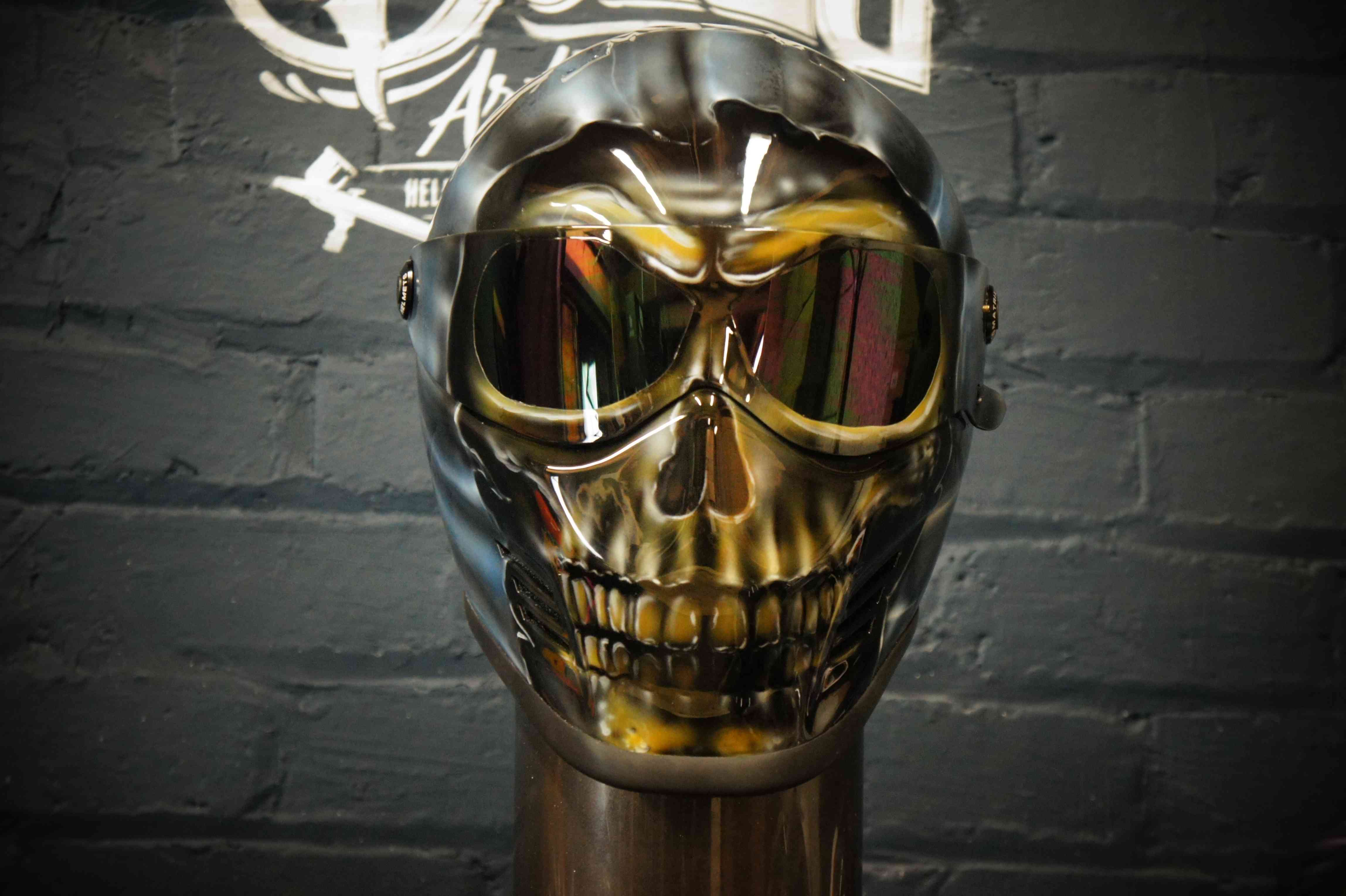 Reflective chrome skull motorcycle helmet with mirrored eye sockets displaying golden tinted reflection and detailed jaw structure