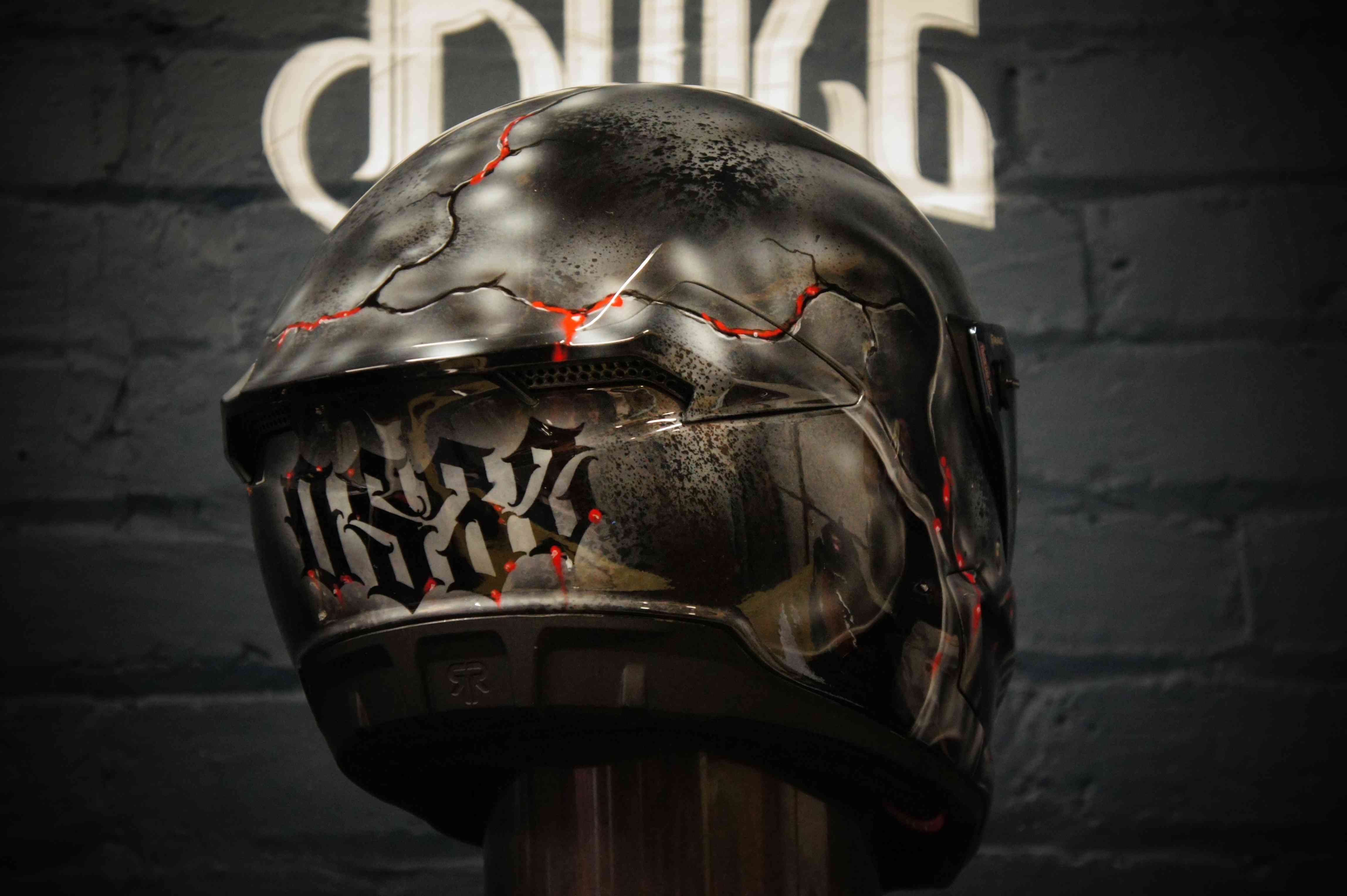Black motorcycle helmet with gothic skull design featuring cracked stone texture, red glowing cracks and ornate lettering