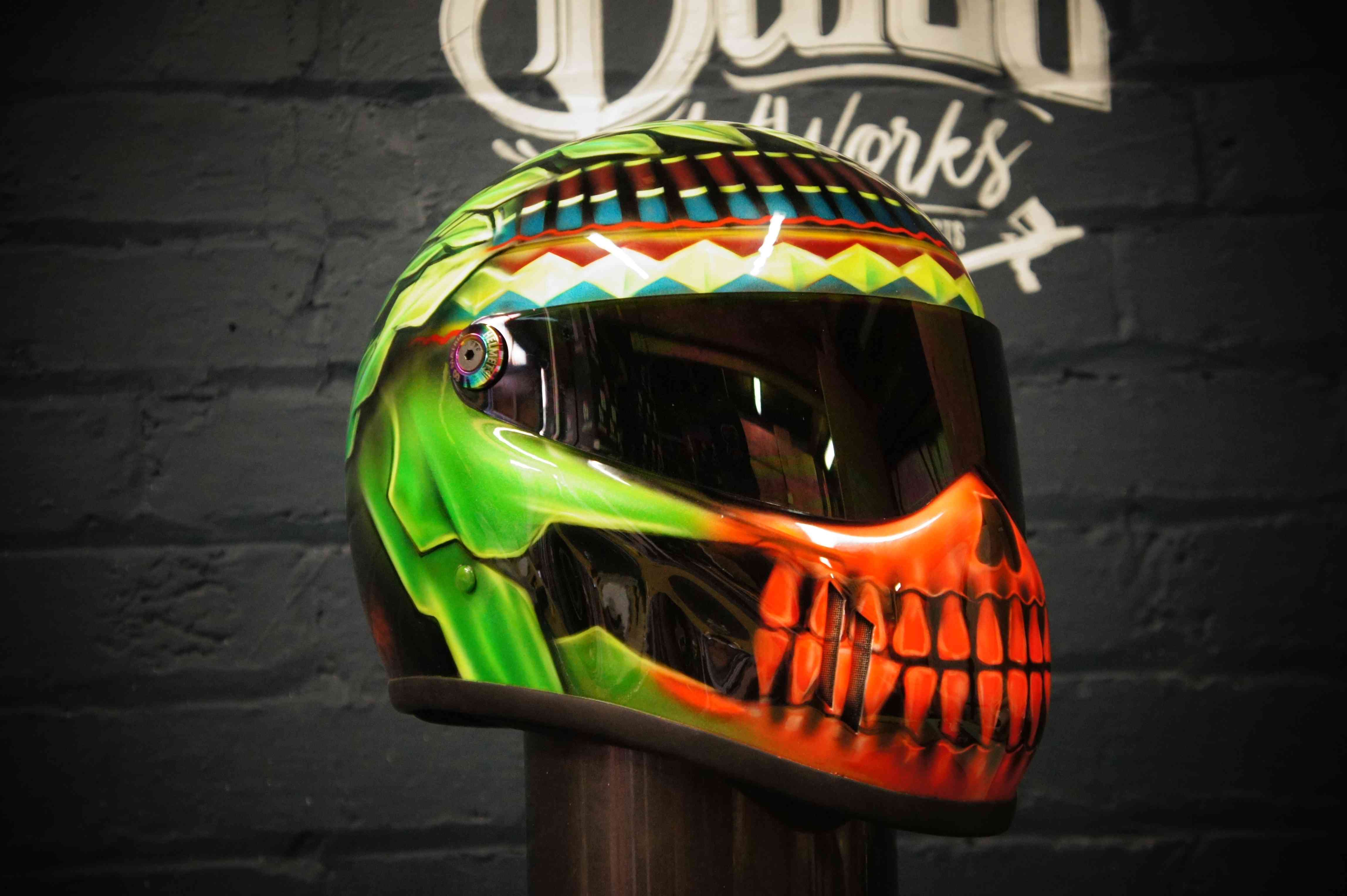 Custom painted motorcycle helmet featuring vibrant green and orange skull design with detailed teeth and jaw, tribal geometric patterns on top