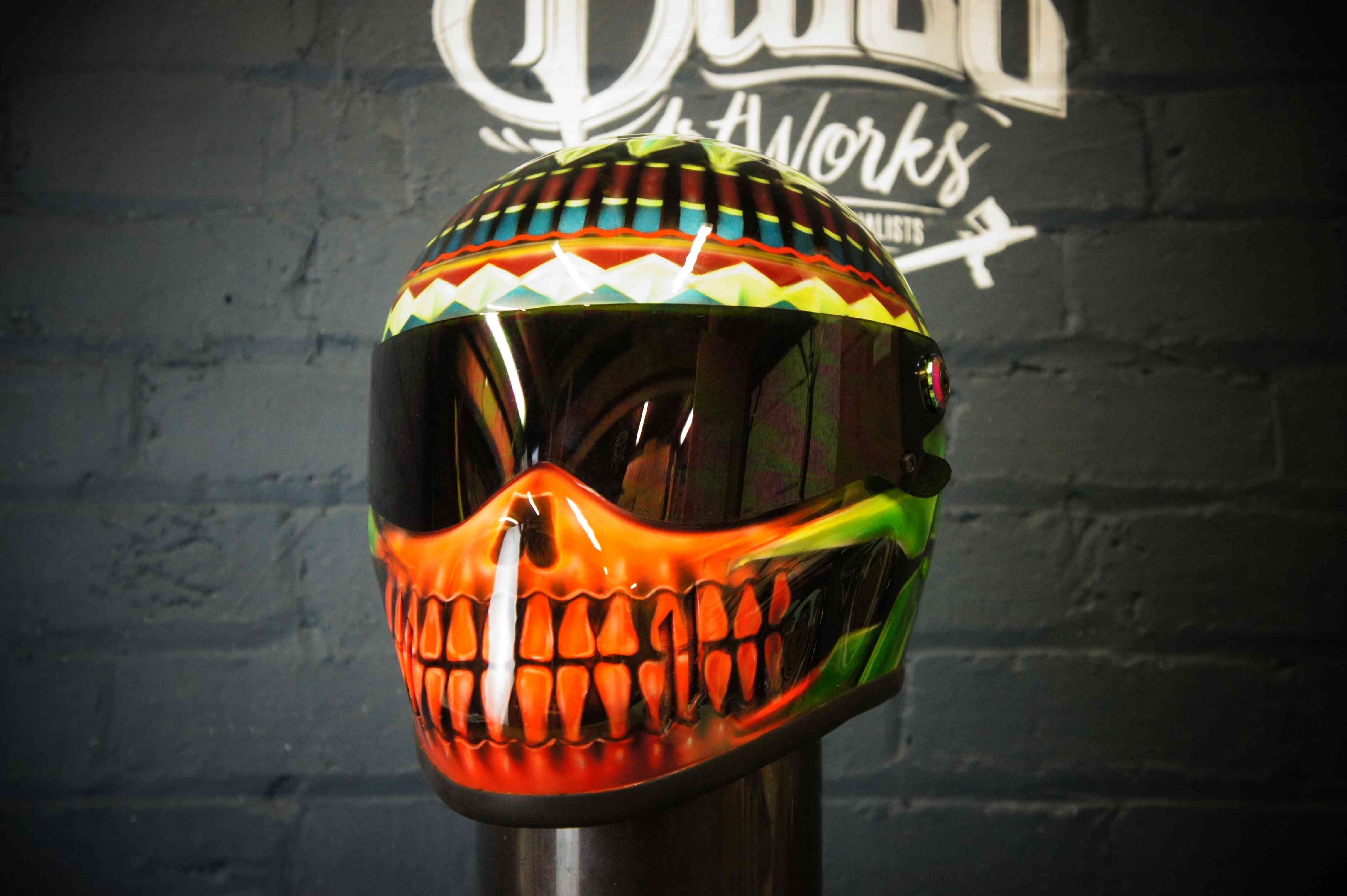 Vibrant skull motorcycle helmet with orange teeth design, tribal patterns on top, geometric colorful bands around crown