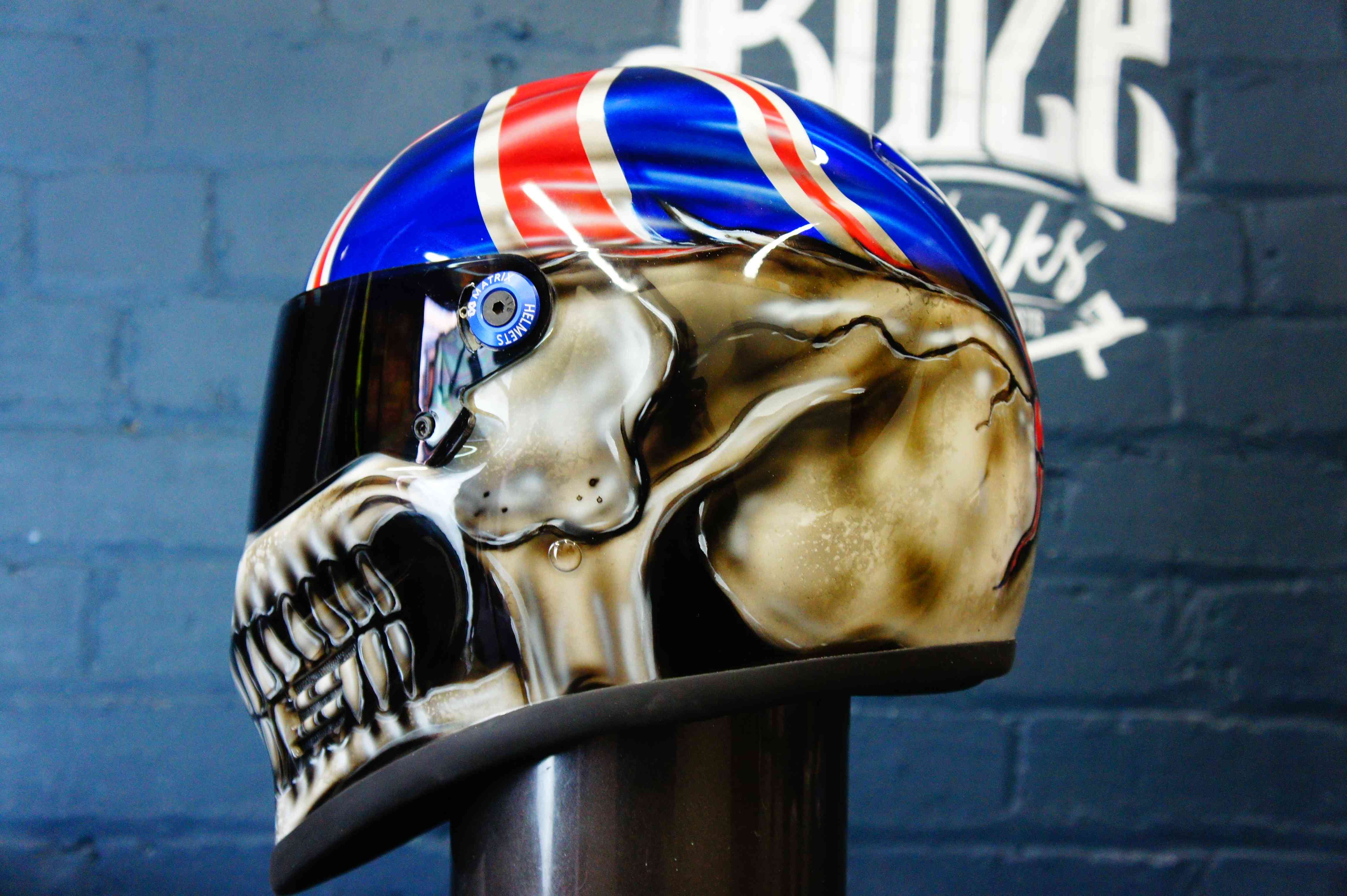 Custom painted motorcycle helmet featuring photorealistic metallic gold skull design with Union Jack pattern on blue background