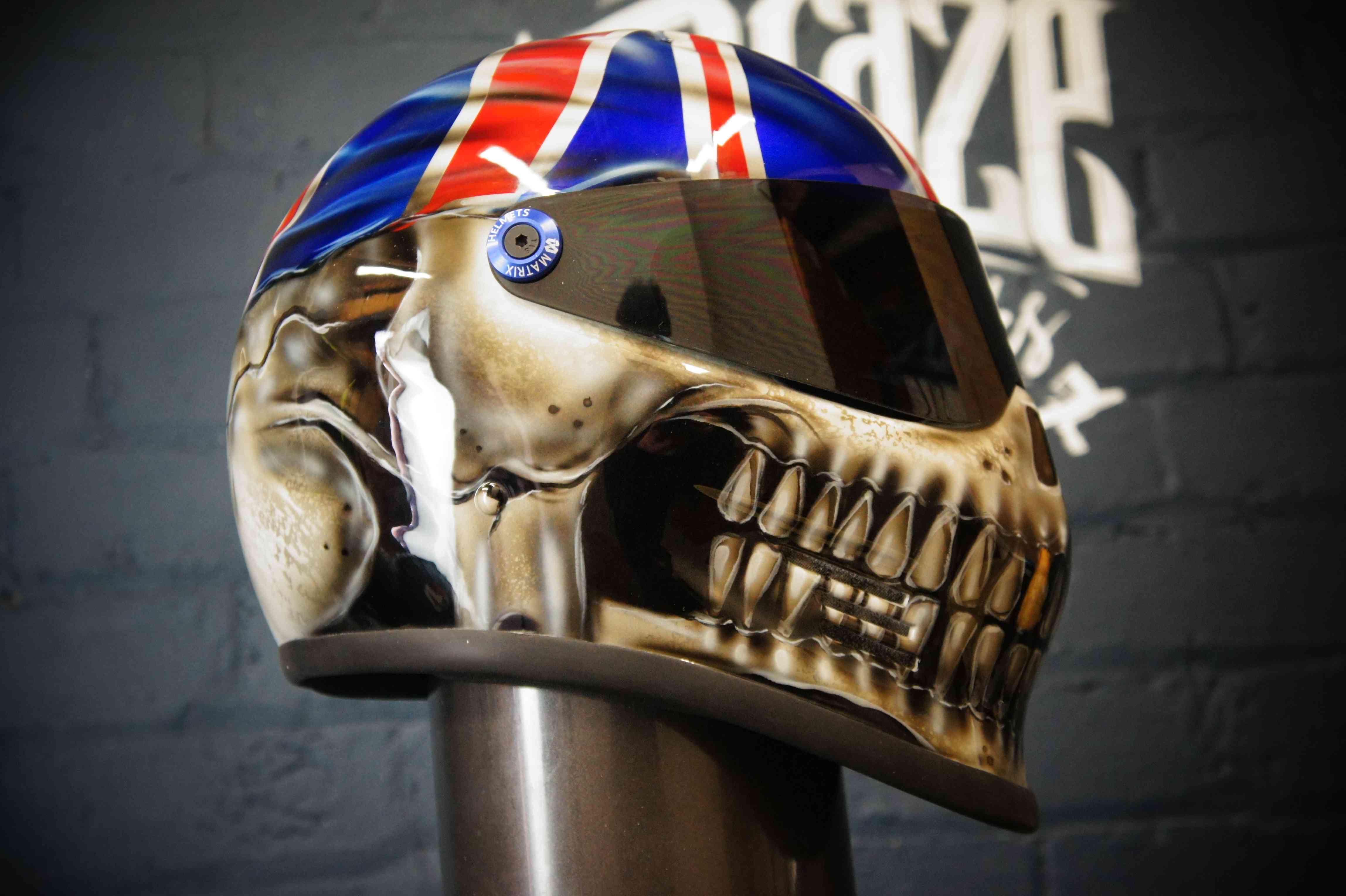 Realistic skull motorcycle helmet with Union Jack flag design on top, detailed anatomical features, metallic finish, visor