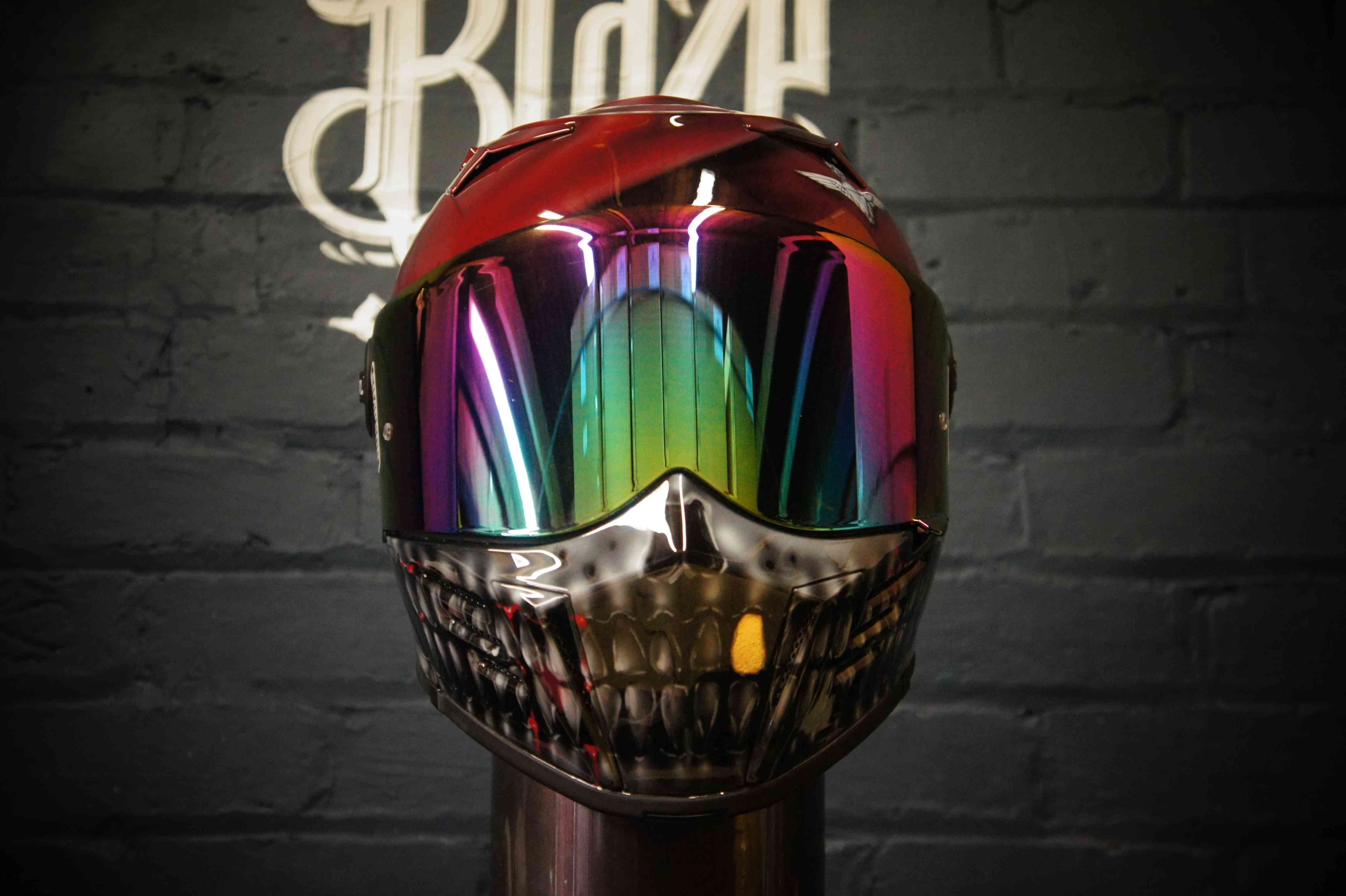 Red motorcycle helmet featuring chrome skull jaw design with iridescent rainbow visor and metallic silver airbrush finish