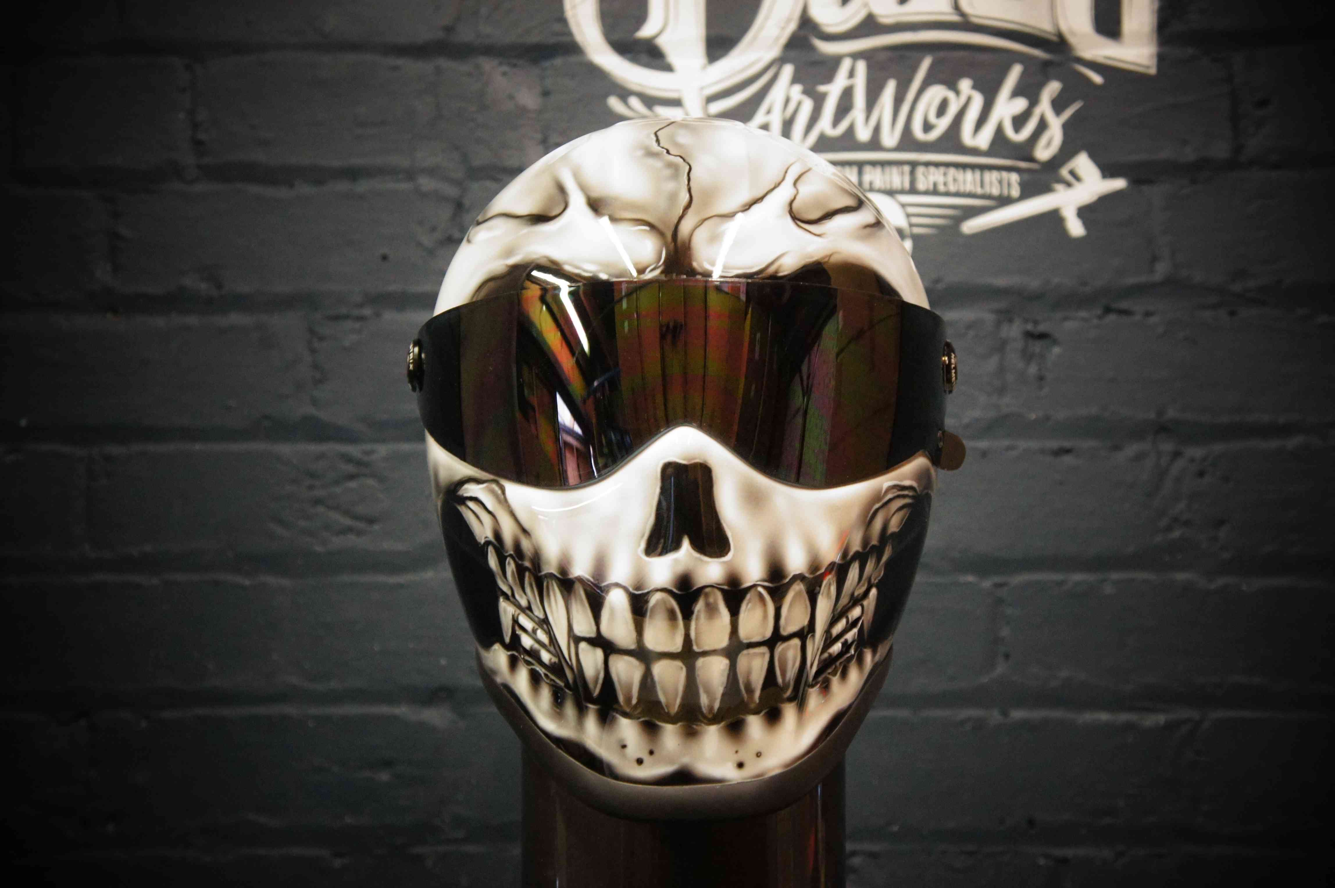 White motorcycle helmet painted with realistic grinning skull design featuring detailed teeth and bone shading effects