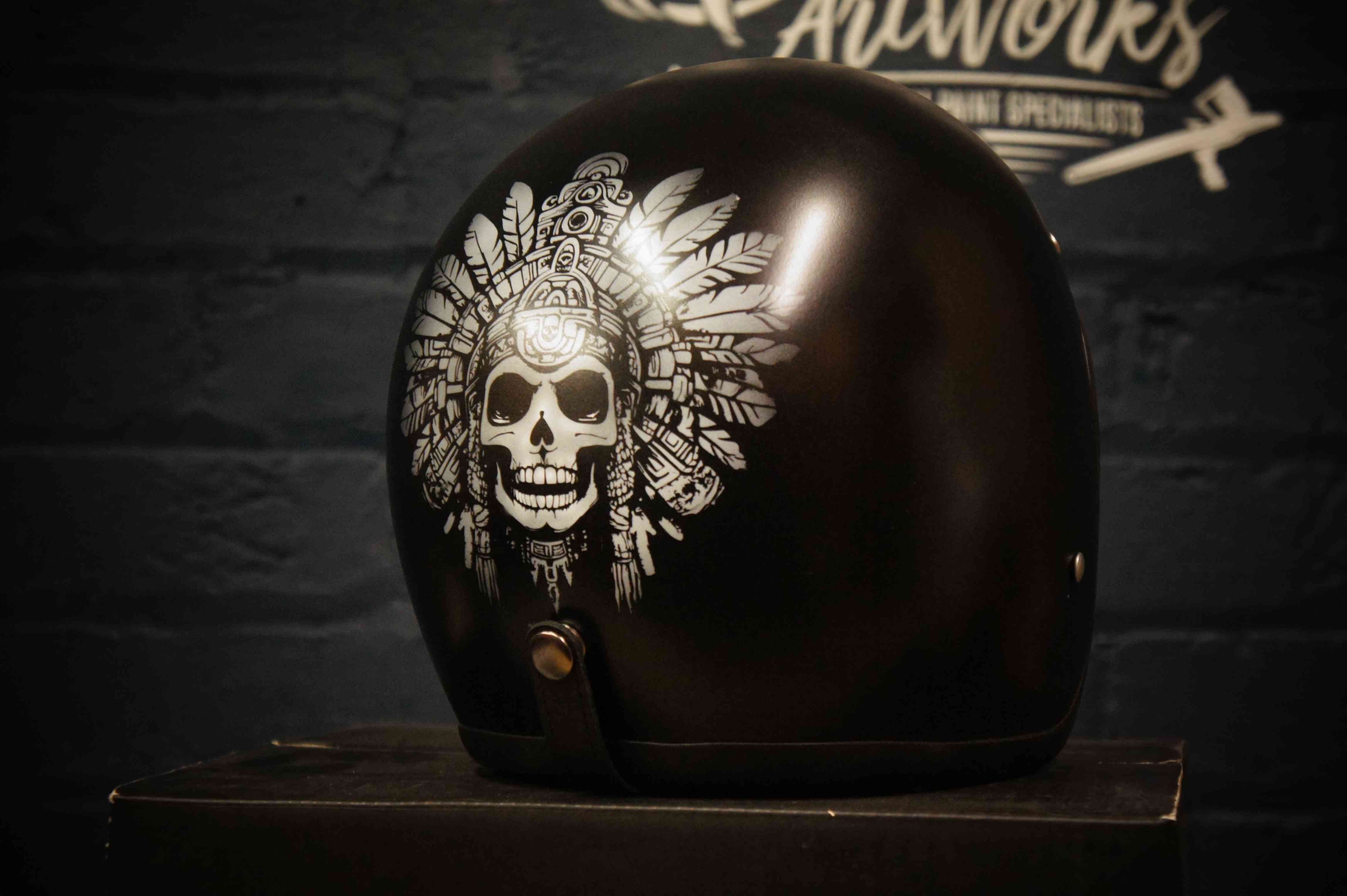Black motorcycle helmet with detailed white skull wearing elaborate Aztec feathered headdress artwork airbrushed on side