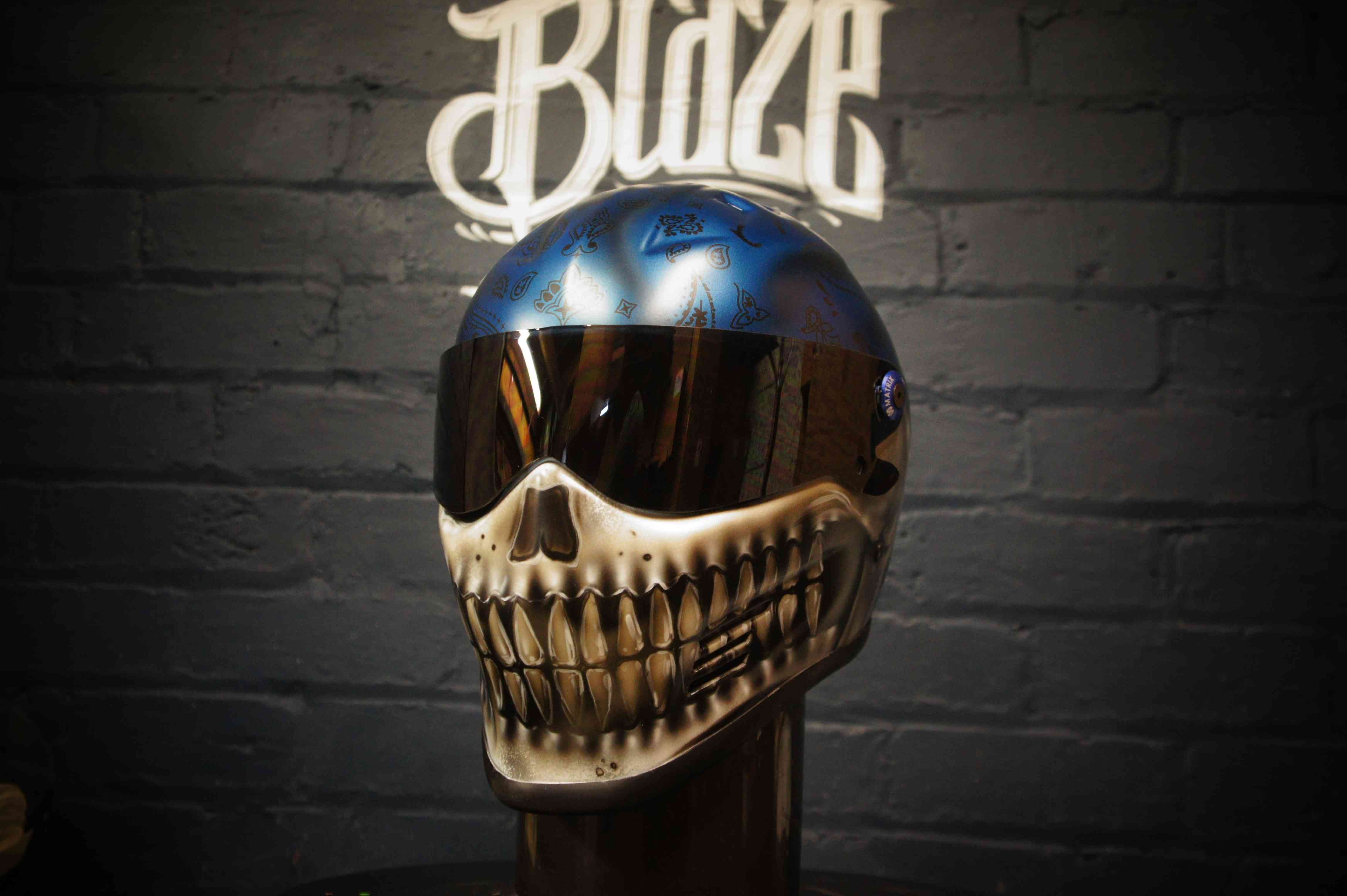 Blue metallic skull motorcycle helmet with realistic bone jaw airbrush art, golden teeth detail on dark background