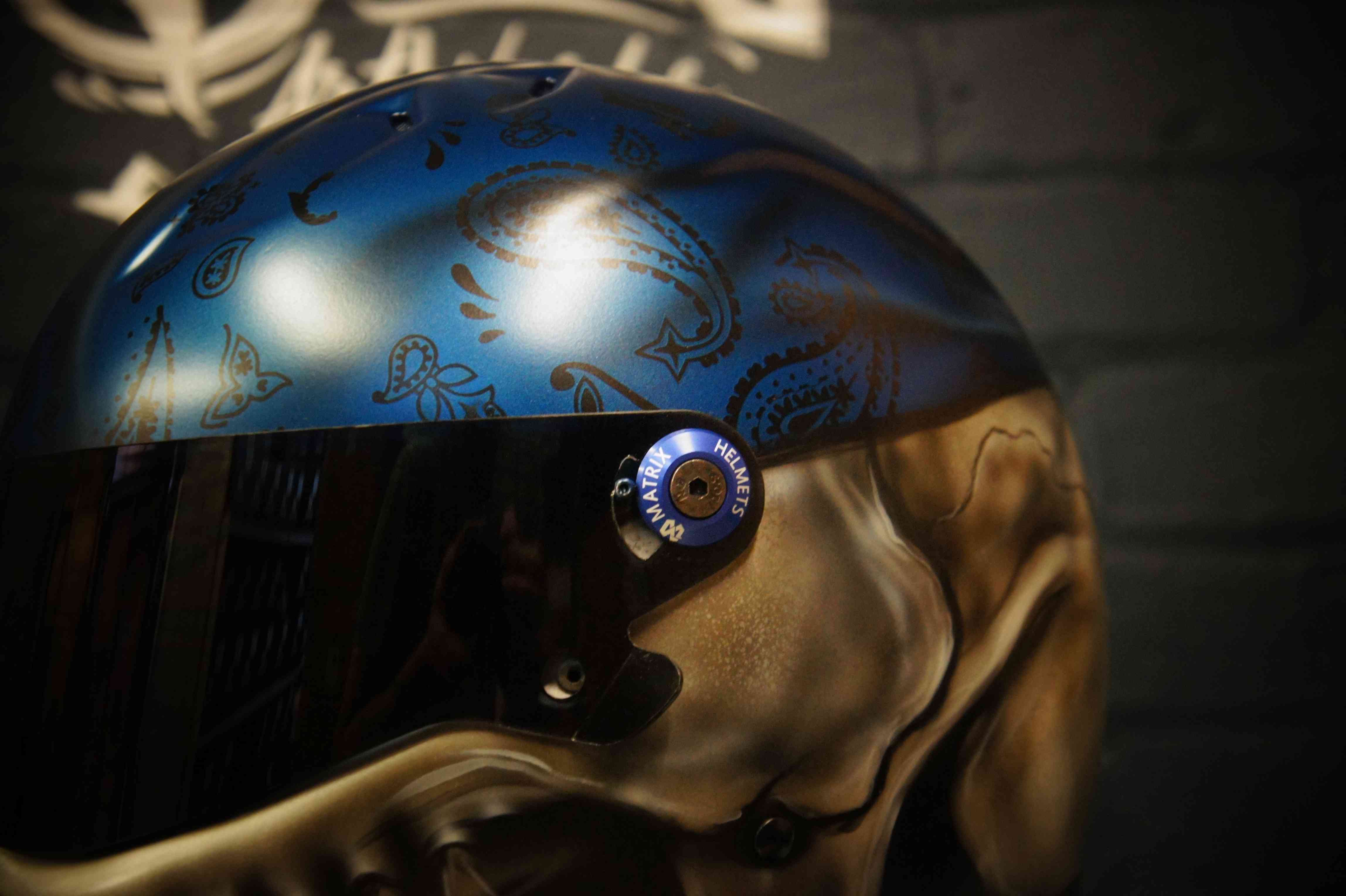 Blue metallic motorcycle helmet with intricate paisley bandana pattern in darker blue tones, featuring teardrop and swirl motifs