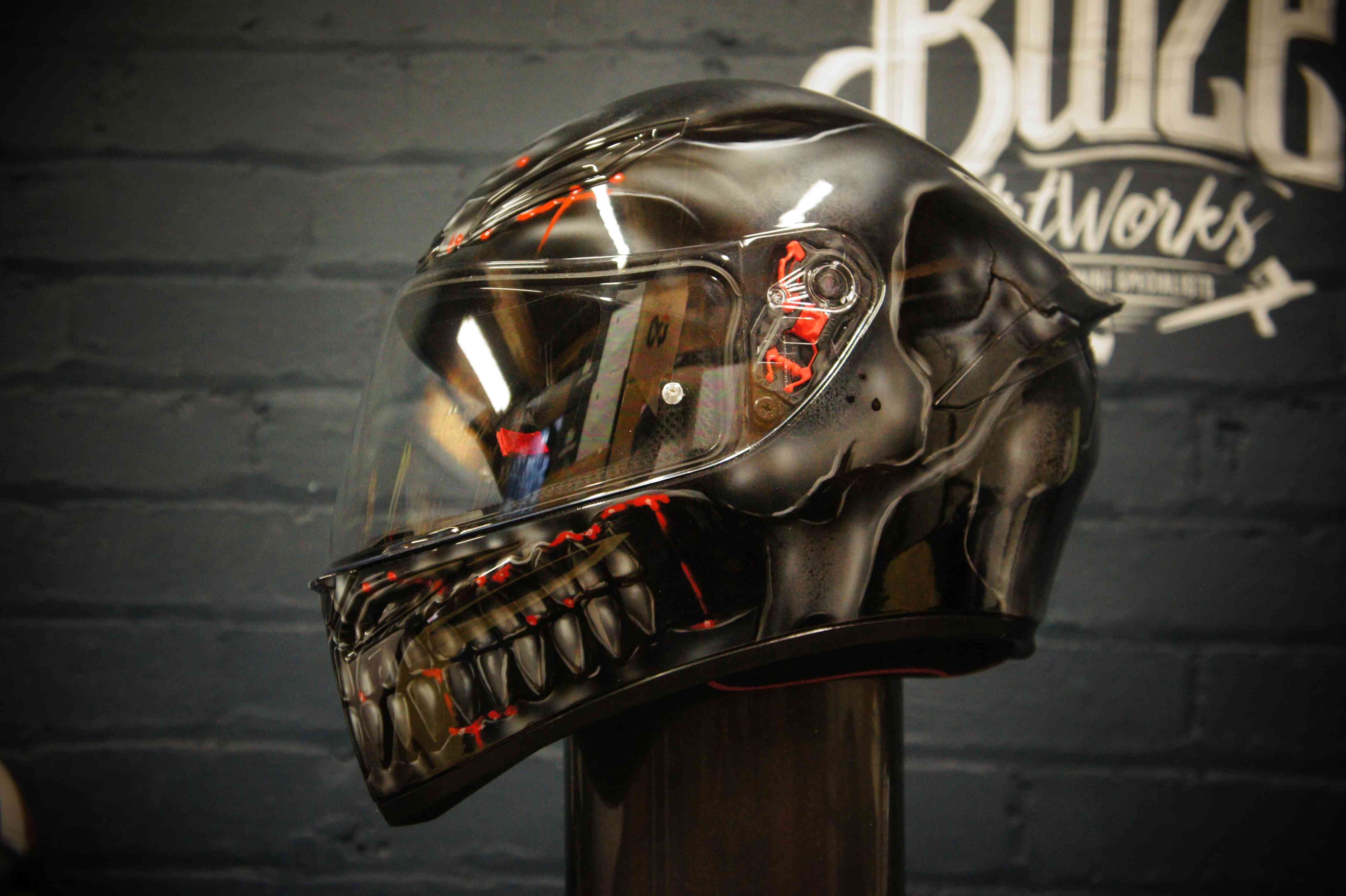 Black motorcycle helmet with metallic chrome skull design featuring glowing red cybernetic eye details and robotic jaw teeth