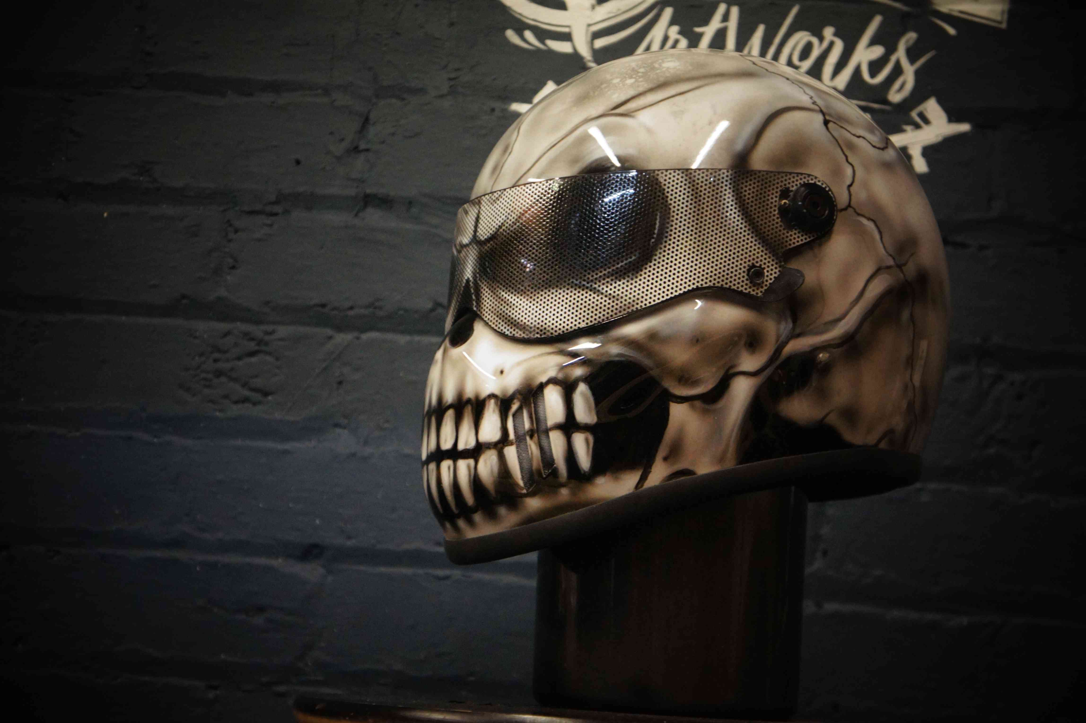 Cream colored motorcycle helmet with airbrushed skeletal skull design featuring mesh goggle effect and exposed jaw teeth