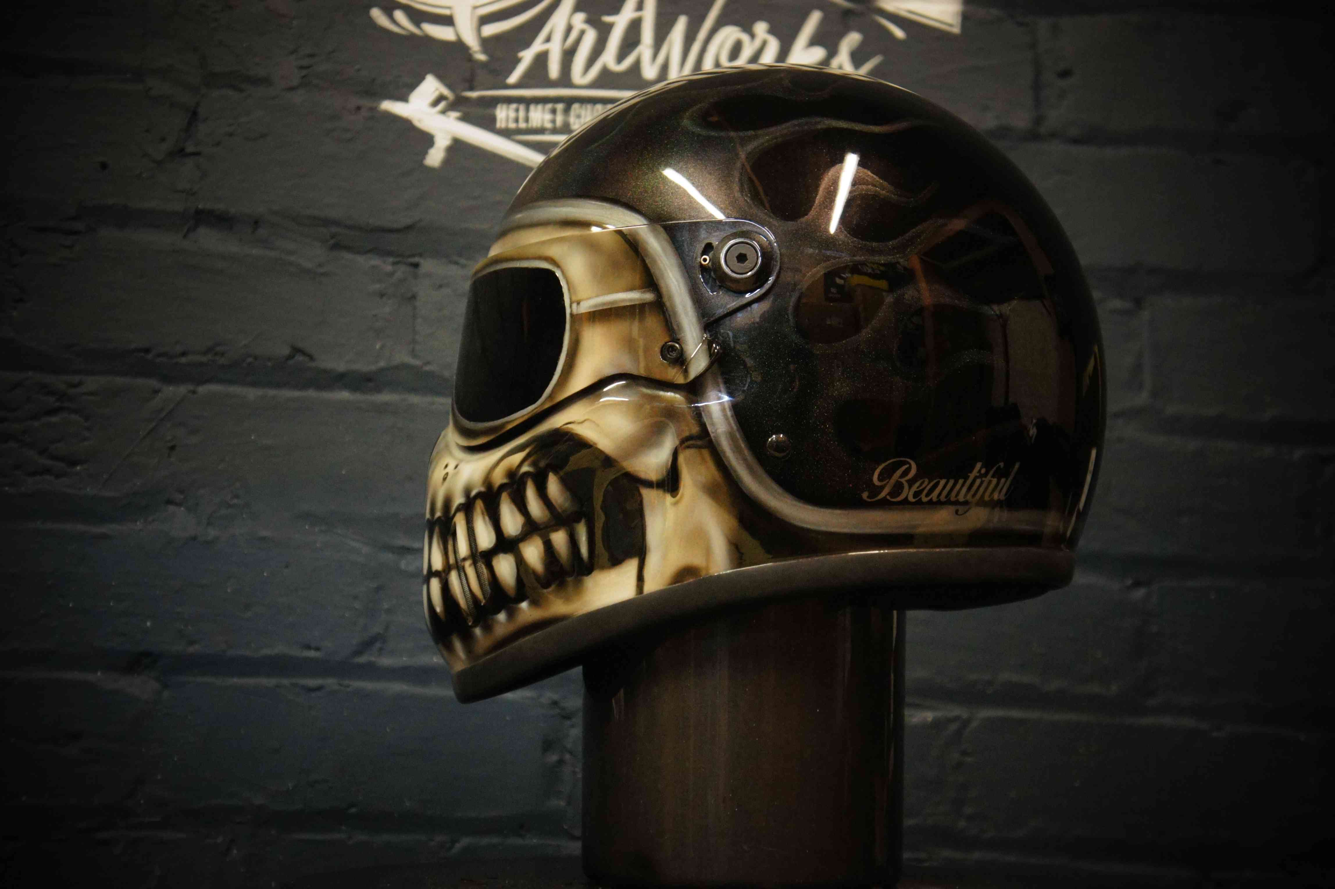 Black motorcycle helmet with realistic skull design airbrushed on side, featuring detailed bone structure and teeth in brown tones