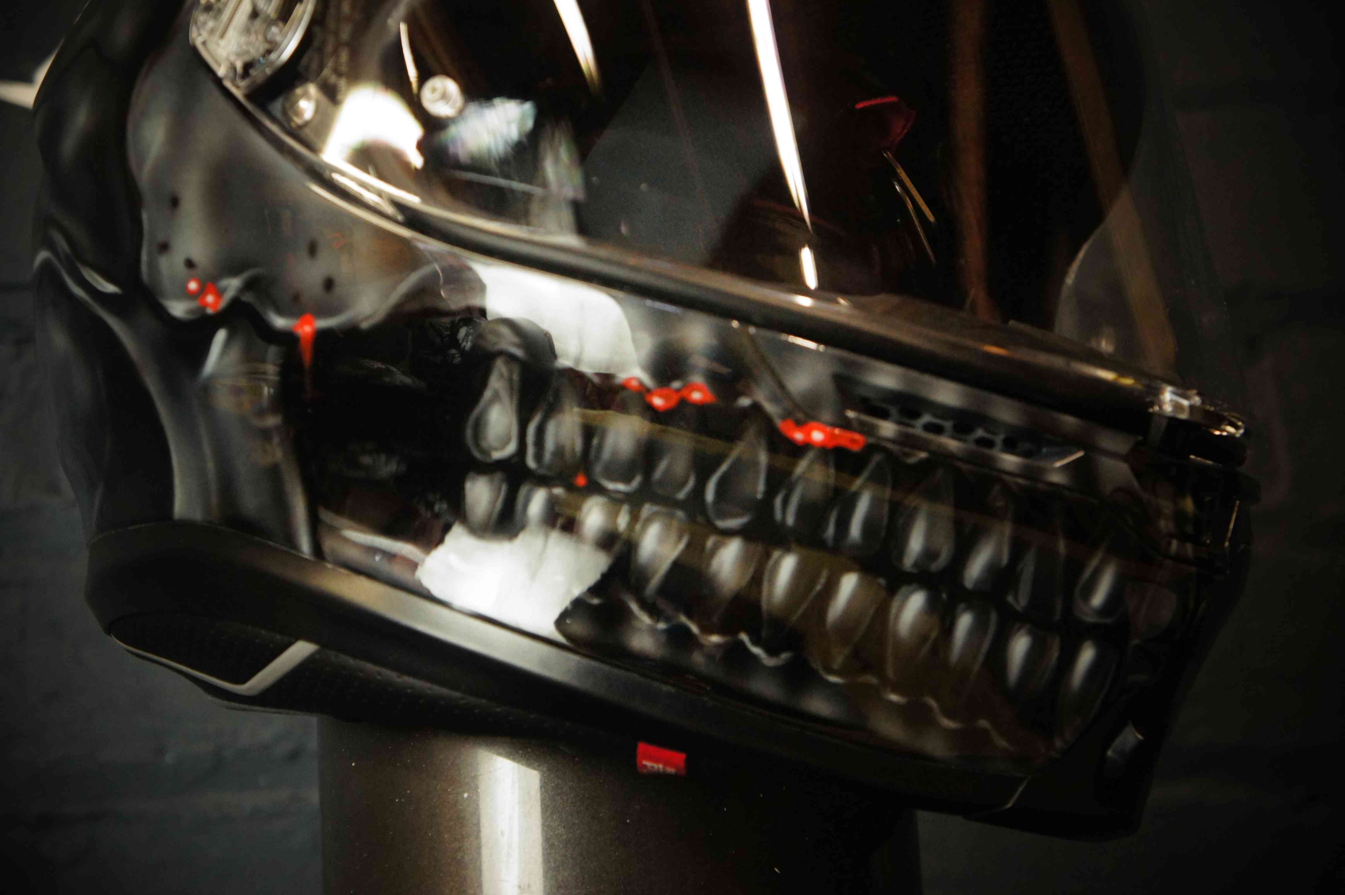 Black motorcycle helmet with detailed grey skull design featuring red glowing eyes and exposed teeth jaw airbrush artwork