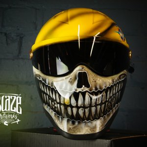 Yellow motorcycle helmet with detailed black and white skull jaw design painted across the face shield area