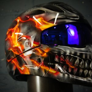 Black motorcycle helmet with orange fire flames surrounding metallic silver skull design, blue tinted visor, professional airbrush