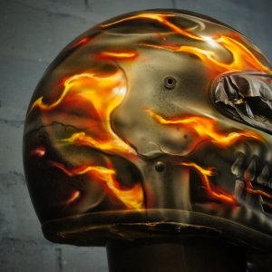 Custom painted motorcycle helmet featuring photorealistic skull design with orange and yellow ghost flames flowing across black surface