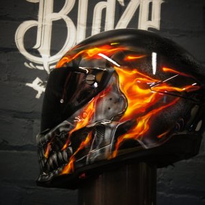 Black motorcycle helmet with realistic orange and yellow flame airbrush design engulfing grey skull artwork on side panel