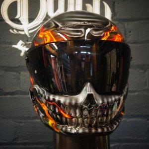 Black motorcycle helmet with orange flame skull design, metallic silver jaw detail, dark tinted visor, professional airbrush work