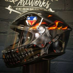 Black motorcycle helmet with airbrushed flaming skull jaw design and glowing orange fire effects on glossy finish