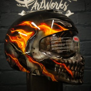 Black motorcycle helmet with realistic flaming skull design in orange and yellow flames, detailed teeth and eye sockets
