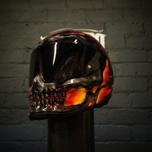 Black motorcycle helmet with photorealistic airbrushed skull design featuring orange and red flame effects around eye sockets