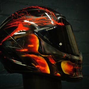 Black motorcycle helmet featuring dramatic red and orange flames with menacing skull face design, glossy professional finish