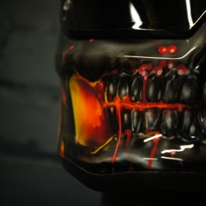 Black motorcycle helmet with menacing skull design featuring fiery orange interior mouth, sharp teeth, and glowing red accents