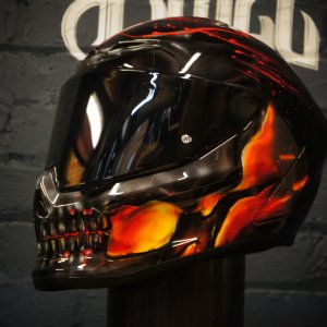 Black motorcycle helmet with realistic orange and red flames surrounding a detailed skull design with glowing eye sockets