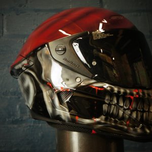 Black motorcycle helmet with photorealistic skull face design featuring glowing red eye sockets and detailed bone structure