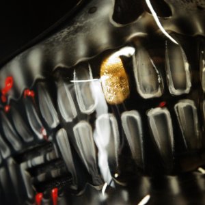 Close-up of motorcycle helmet with realistic 3D skull jaw design in black and gold, showing detailed teeth and bone structure