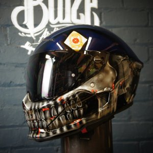 Black motorcycle helmet with photorealistic metallic skull design featuring glowing red accents and anatomical detail work