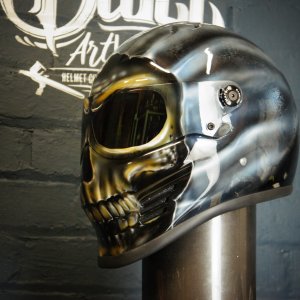 Chrome silver motorcycle helmet with airbrushed skull jaw design featuring golden eye sockets and realistic bone detail